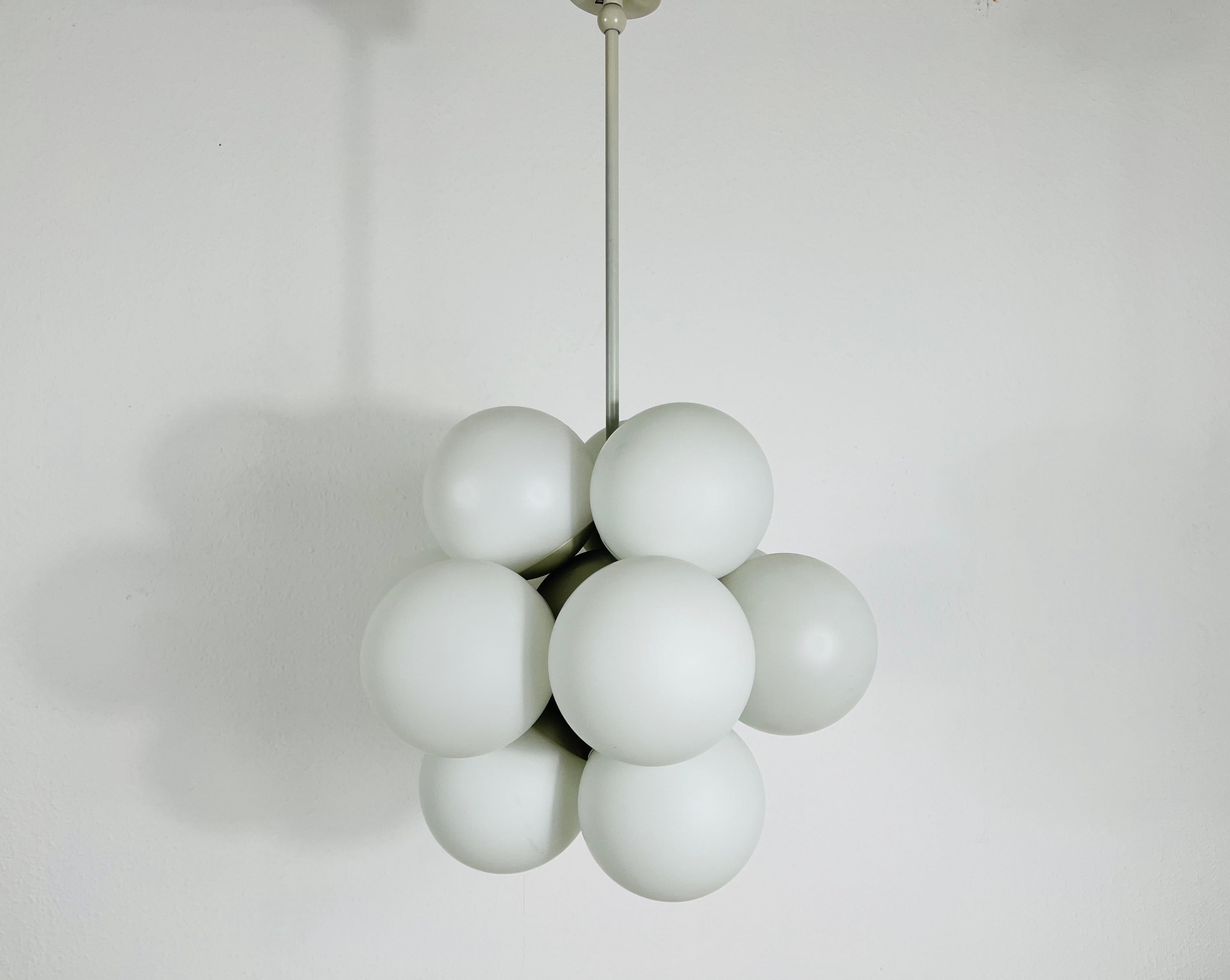A midcentury chandelier by Kaiser made in Germany in the 1960s. It is fascinating with its Space Age design and twelve opaque balls. The white circular body of the light is made of full metal, including the arms. White bar with white