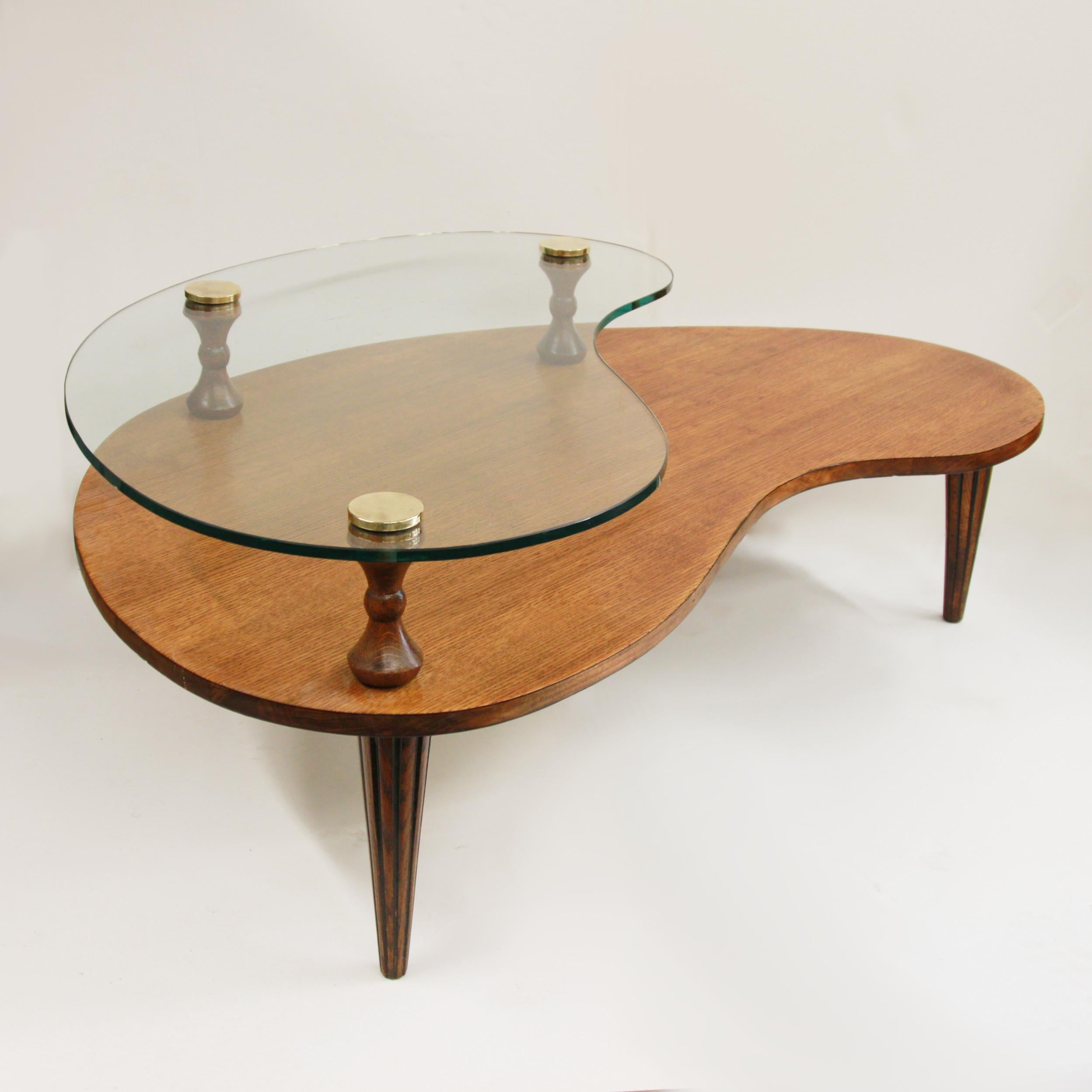 Fantastic biomorphic/kidney shaped coffee table attributed to Gilbert Rohde for Herman Miller.  

Table features:

- Two-tiered top
- Tapered oak legs with fluting
- Turned oak risers
- Solid brass screw-caps

This is a high-quality, high-style
