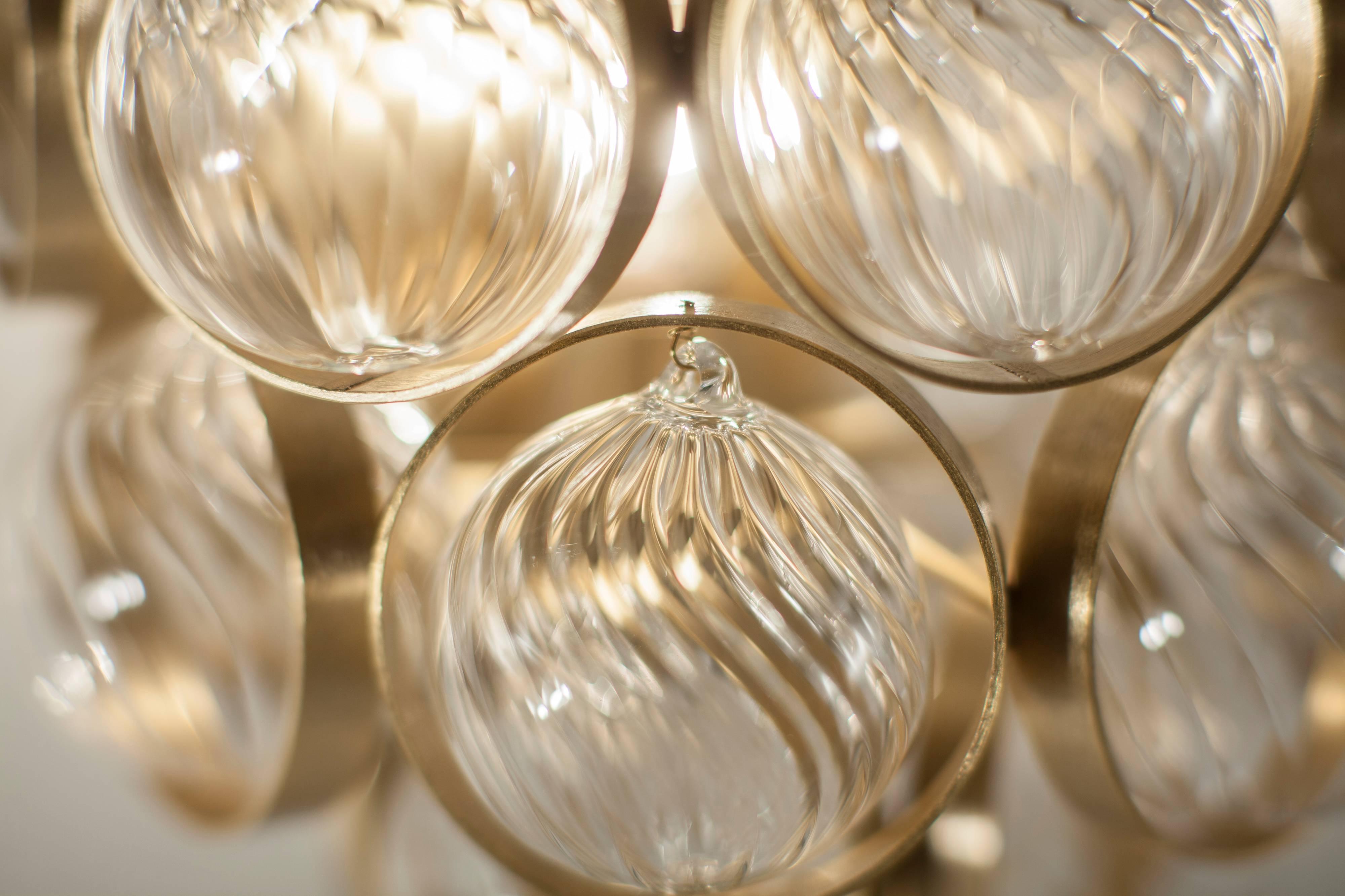 With satin gold metal and handblown clear glass spheres with spiral ribbing, the Atomos is symmetrically aligned but also has a rich vitality and brightness to it. Each textured glass ball within this lively cluster is held within a flat metal ring