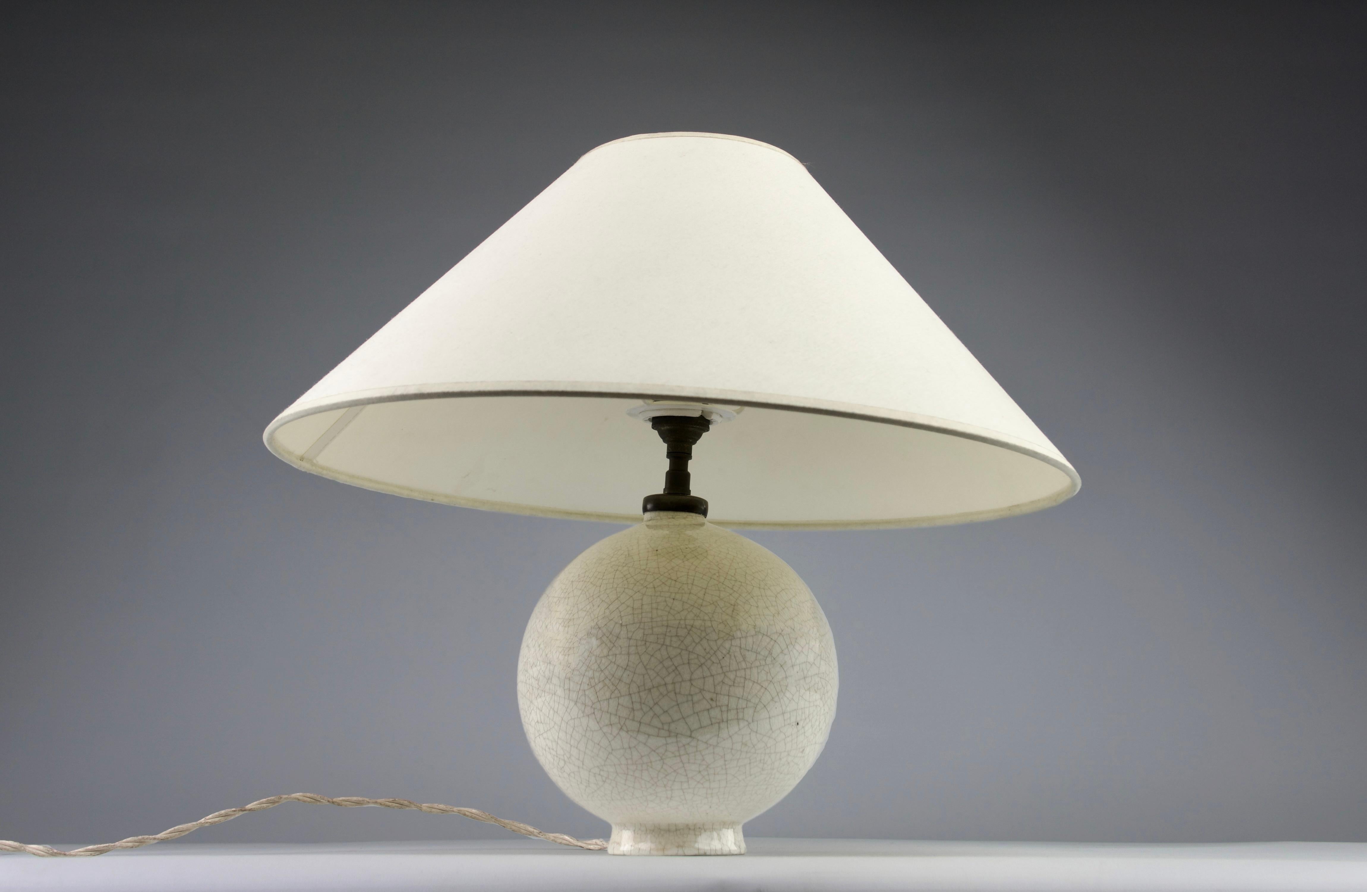 Elegant table lamp with a spherical ceramic body. White crackled enamel decor. Art-Deco, neo-classic, Modernist. Attributed to Jean Besnard. 

Stamped STR France, 1930. 

Dimensions (H x D) in cm: 23 x 15

Great and working