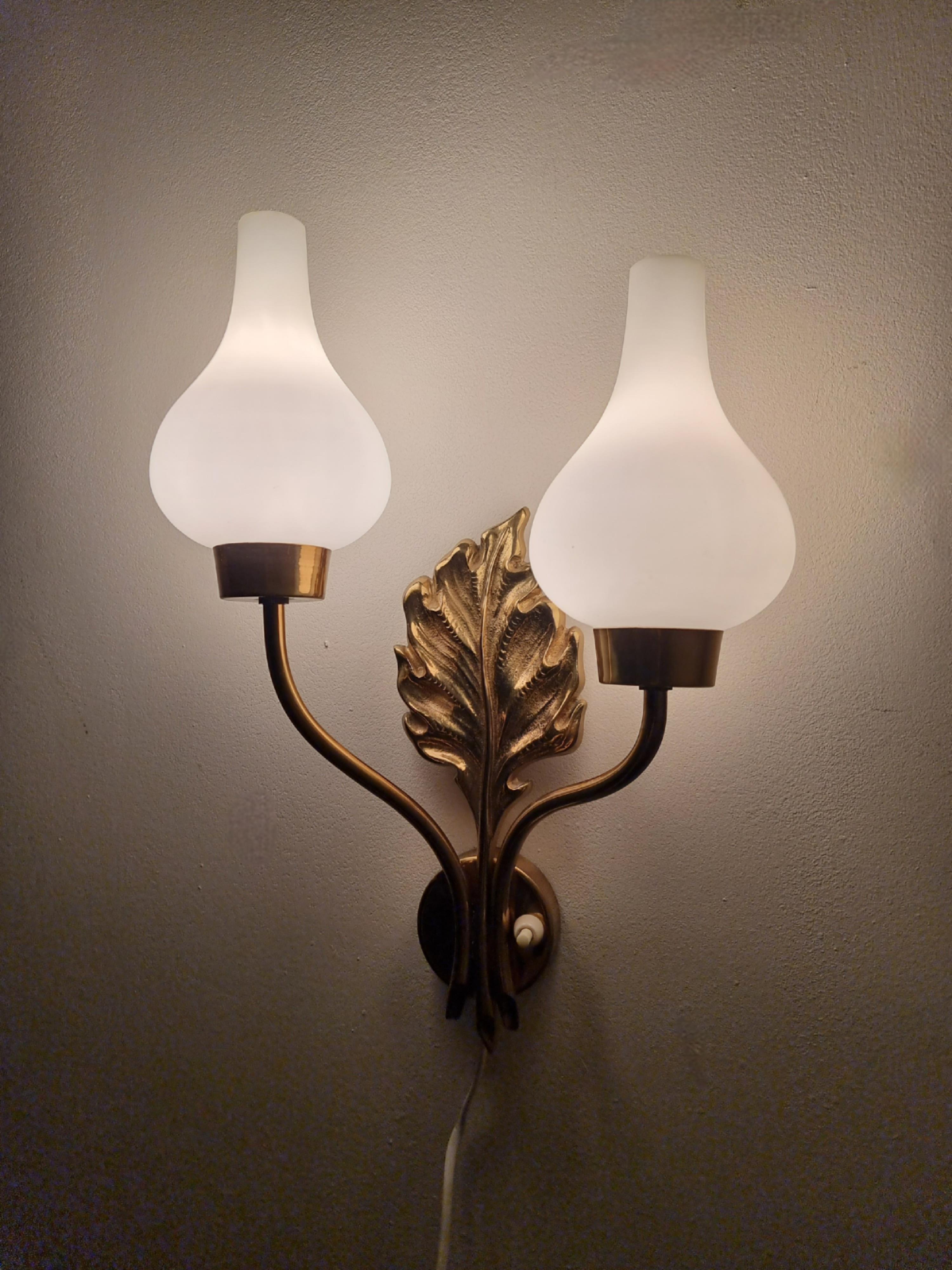 A pair of rare, sculptural wall fixtures in solid brass with glass shades. In the manner of swedish designer Einar Bäckström. Decor of leafs, the white glass shades gives a nice, comfortable shine. 

In good condition with age related patina and a
