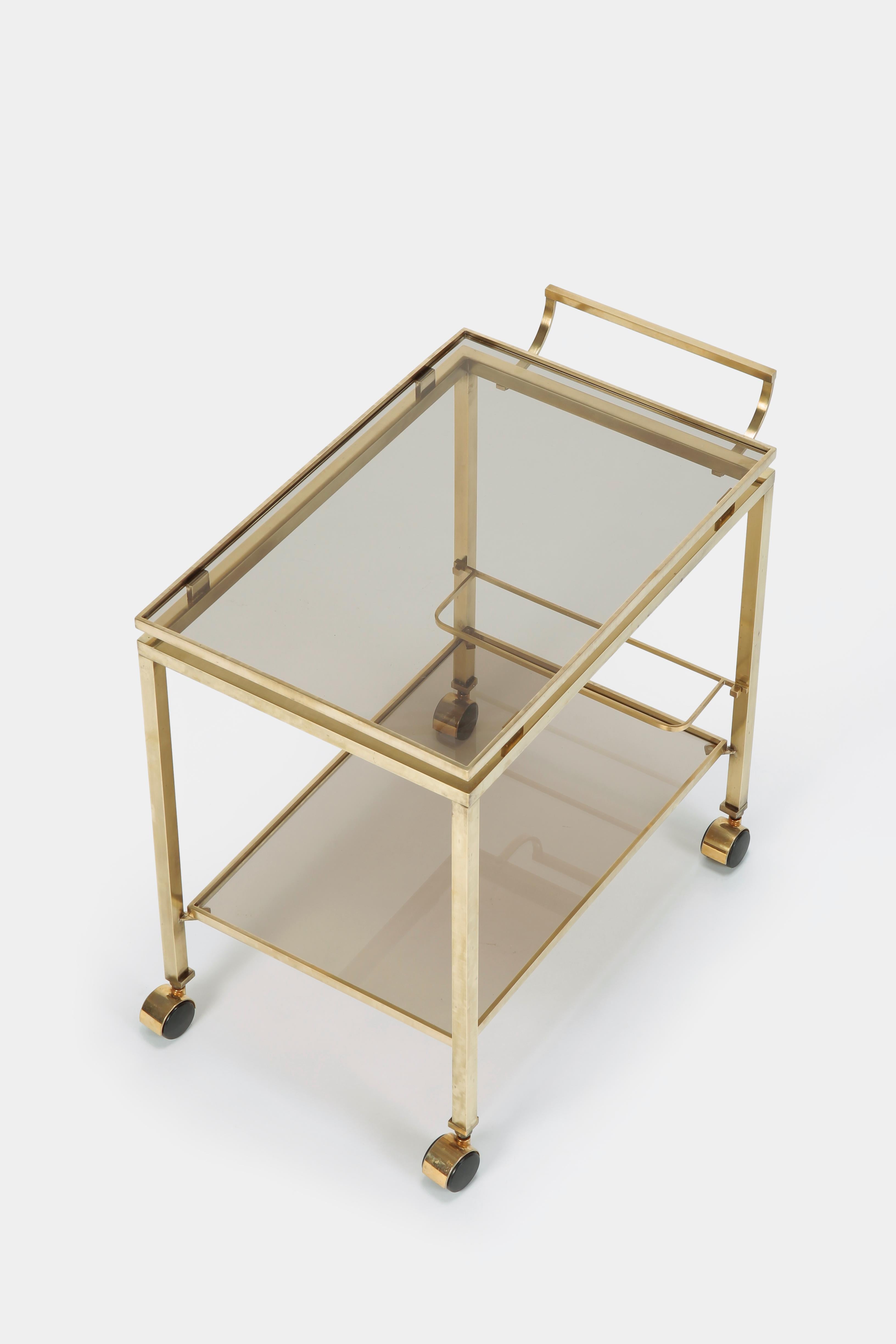 Designed by Guy Lefèvre for Maison Jansen. Serving trolley manufactured the 1960s, Paris, France. Elegant piece made of solid brass and smoked glass. The refined design makes the upper surface appear to float. Beverage holder on the bottom shelf.