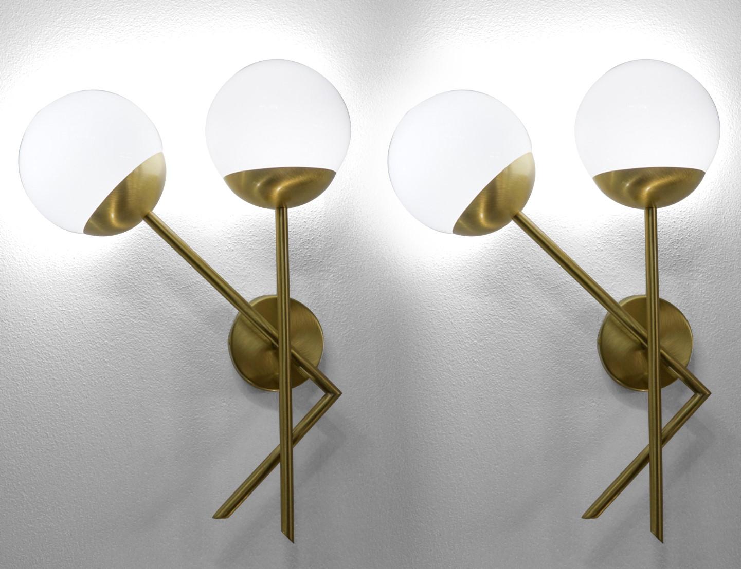 Definitely a minimal applique, in which the satin brass color finish is the protagonist of this magnificent product. 
It supports two milky white glass spheres that light up creating a soft and delicate light. 
In fact, inside the two glass