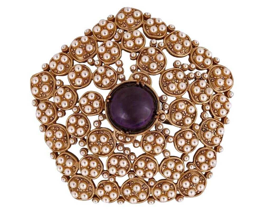 A vintage golden cluster brooch with small round white glass jewels and a large central purple stone. The piece presumably belongs to a collaboration between Chanel and Atelier Gripoix. Gripoix glass is poured directly onto a jewelry piece to create