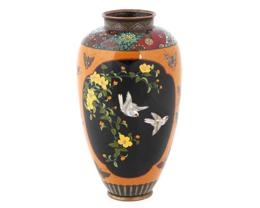 Antique Japanese, late Meiji era, enamel over copper vase. The vase has an urn shaped body and a wide neck. The body of the vase is adorned with polychrome medallions depicting birds in blossoming flowers and plants made in the Cloisonne technique.