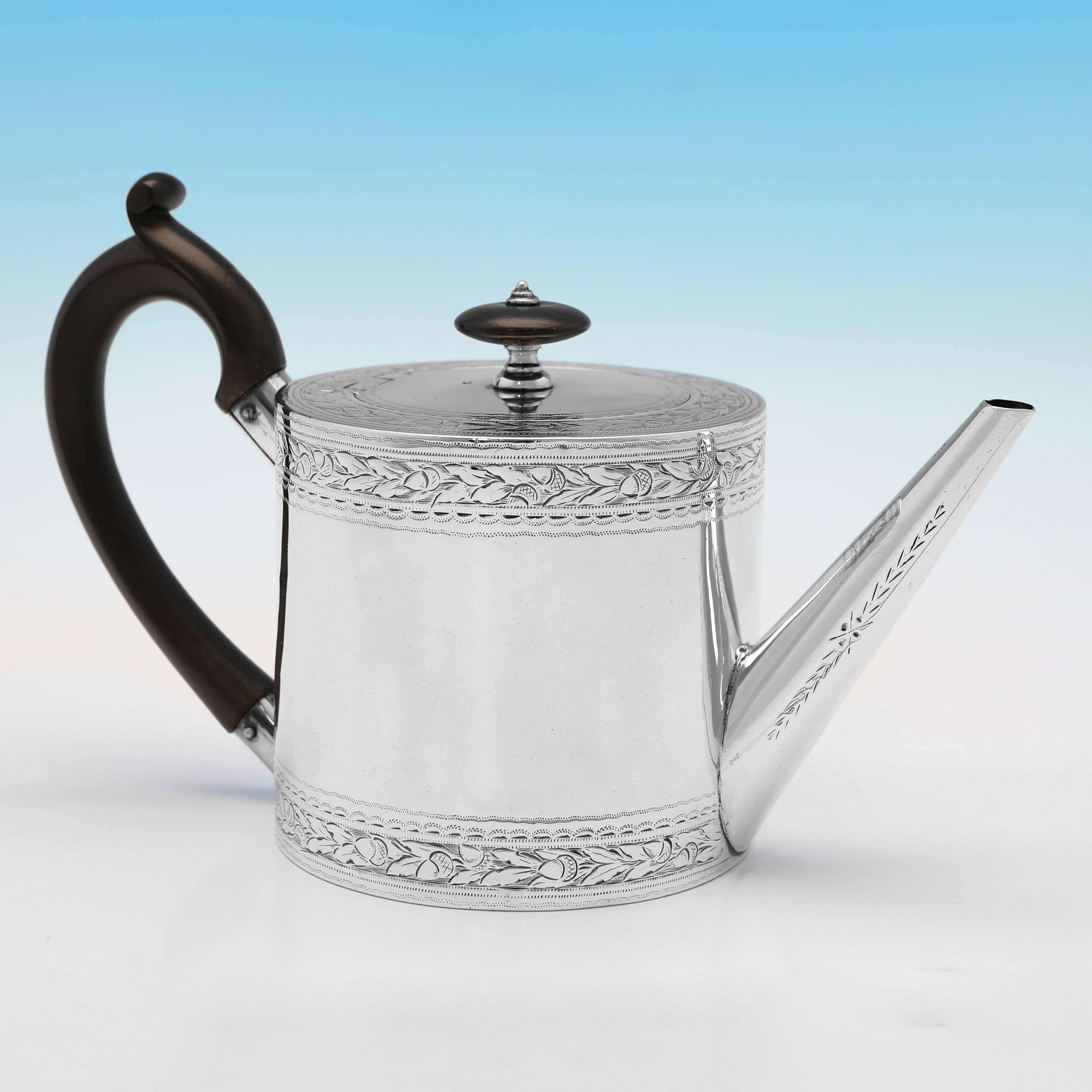 Hallmarked in London in 1798 by John Emes, this attractive, George III, Antique Sterling Silver Teapot, is 'Drum' shaped, and features engraved decoration throughout, and a wooden handle and finial. 

The teapot measures 4