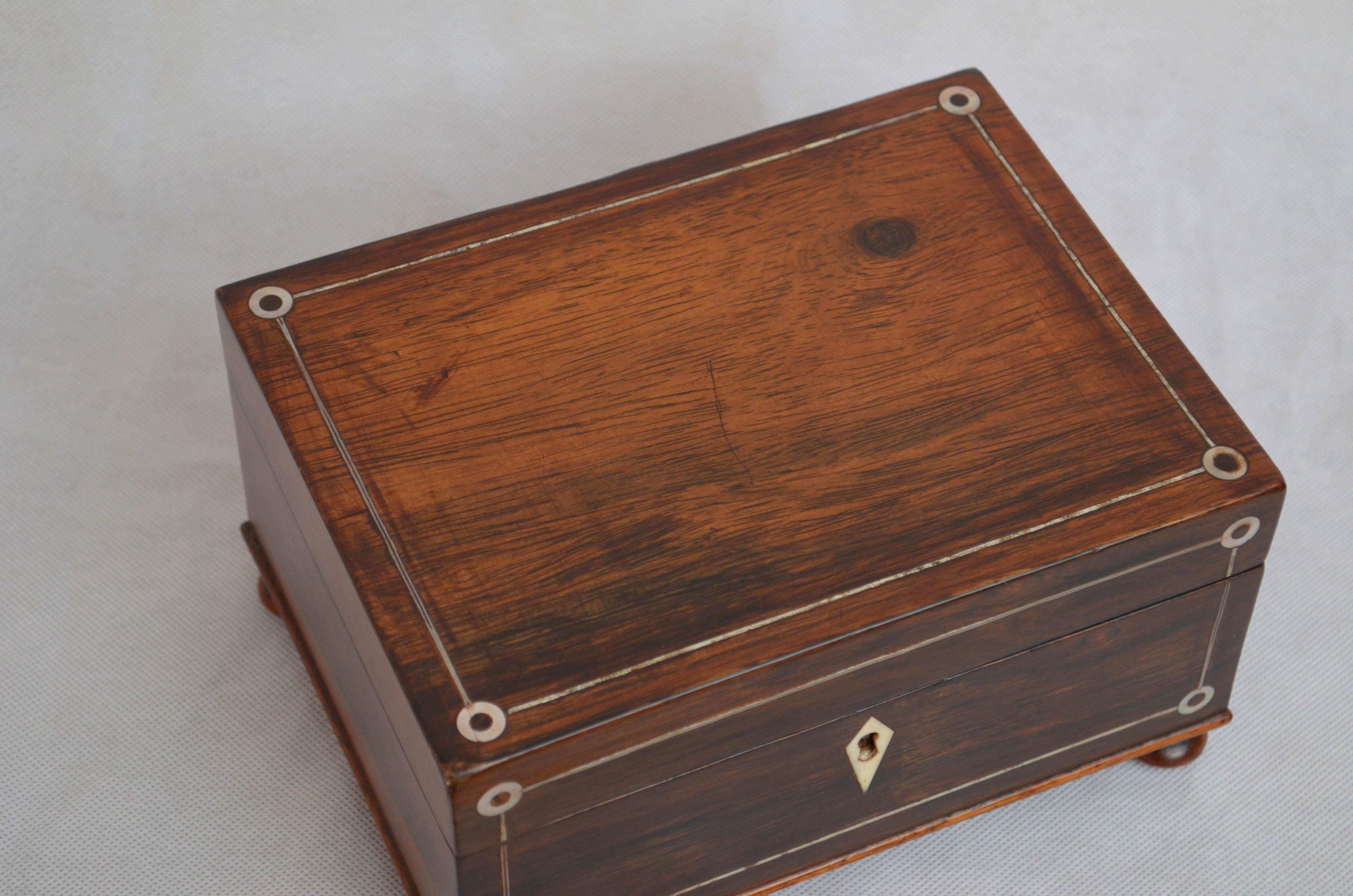 Very attractive rosewood sewing box or jewelry box with decorative metal and mother of pearl inlays and hinged top which opens to reveal clean relined interior with lift up tray, all standing on bun feet. This antique box has been sympathetically