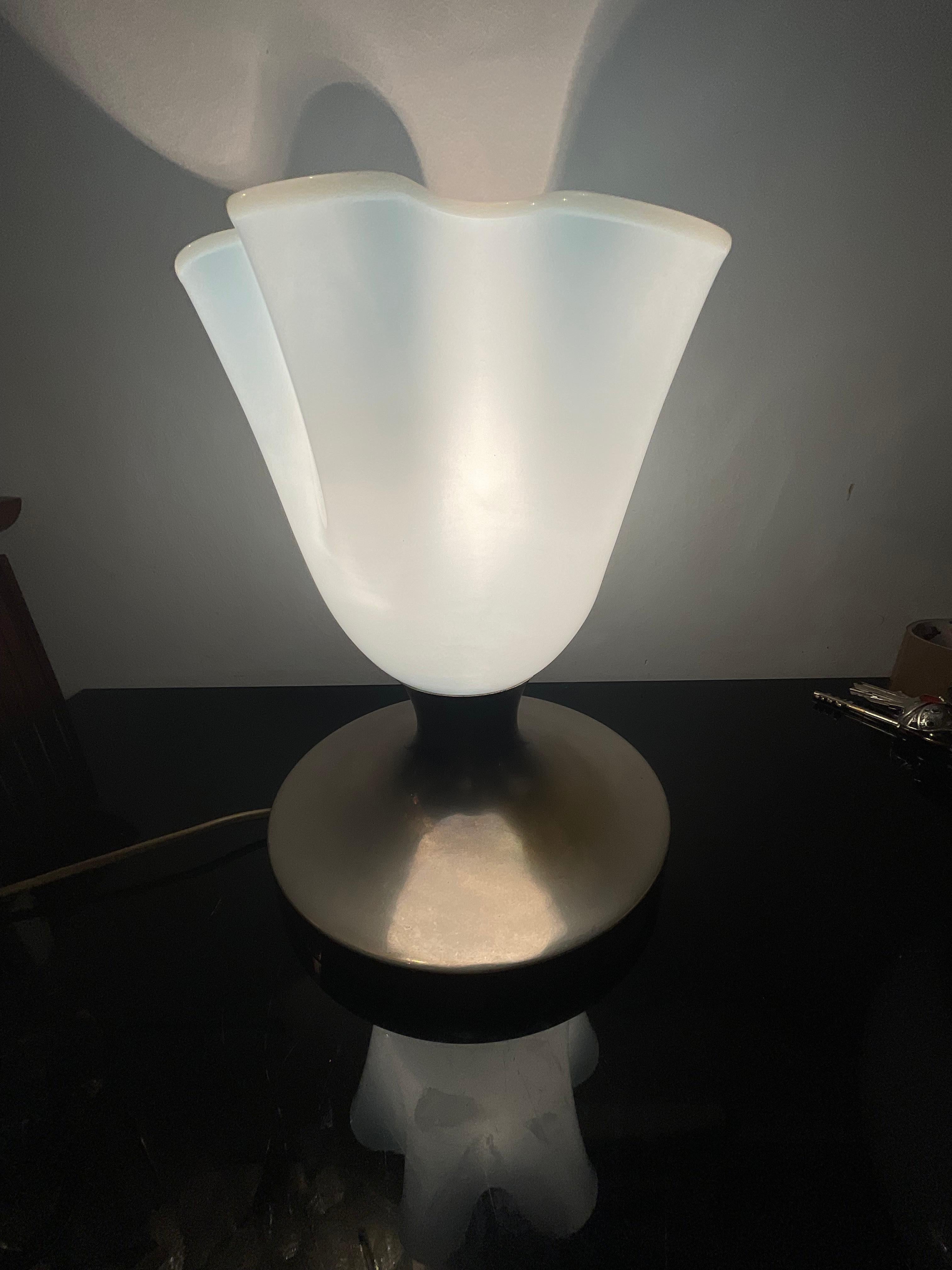 Rara lampada da tavolo anni 50, attribuita a VENINI probabilmente disegnata da Fulvio bianconi e Paolo Venini, negli anni 40.
Il fazzoletto in vetro di murano e colore azzurro tenue con il bordo più chiaro , la base e in ottone cromato.
La lampada è