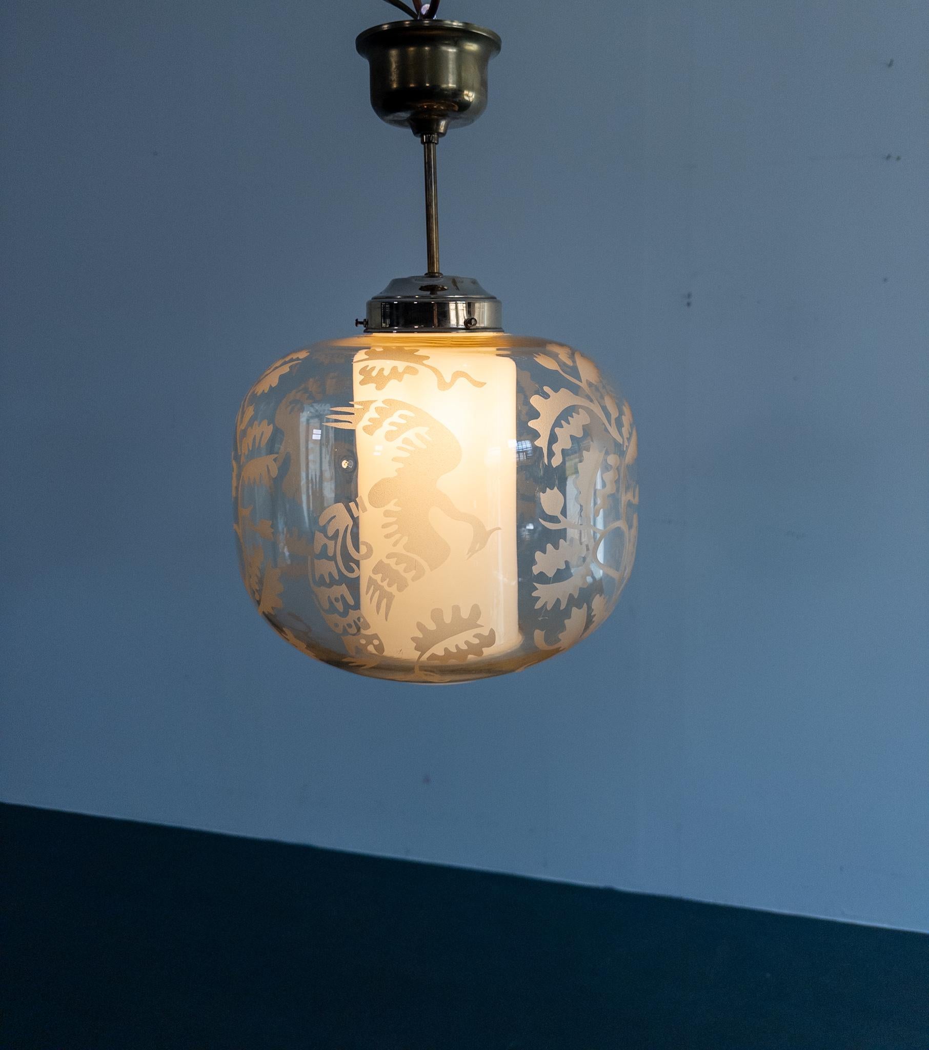 Elegante lámpara colgante sueca, atribuida a Arvid Böhlmarks Lampfabrik, hacia 1930. El globo de cristal transparente está ricamente decorado con motivos arenados de pájaros volando y hojas de roble estilizadas, creando un sorprendente juego de