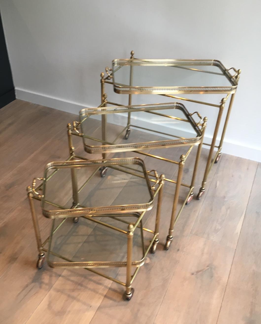 This set of 3 neoclassical style nesting tables on casters are made of brass. These trolleys have fluted legs, decorative finials and very fine removable trays. The quality of these pieces is really fine. This is a work by famous French Maison