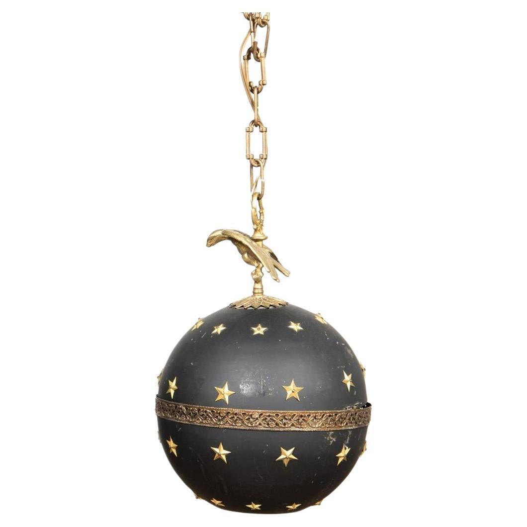 Attributed Maison Jansen (French), second half 20th century. Spherical-form black tole ceiling light fixture in the empire taste, surmounted by an eagle, having a pierced foliate band, hinged, and decorated with brass stars. Unmarked. Dimensions: