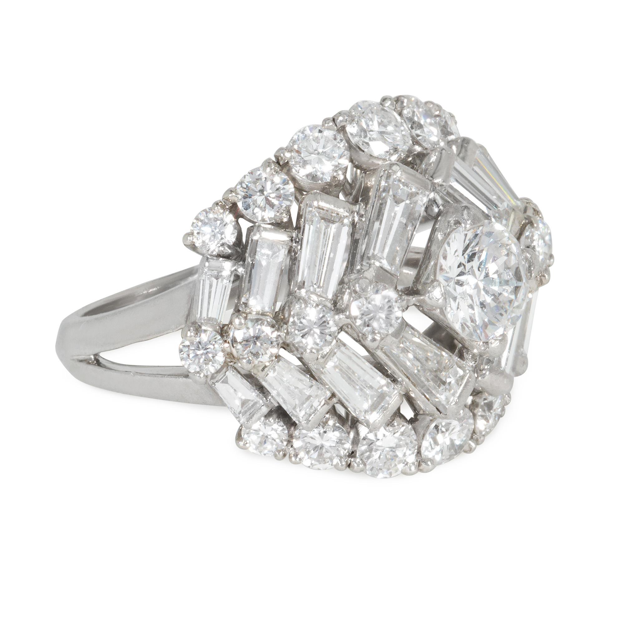 A Mid-Century diamond and platinum ring of opposed herringbone, chevron design comprising tapered baguettes and round brilliant cuts, with a central round diamond, in a stepped platinum mount with pierced under gallery.  Atw diamonds 3.00 cts.