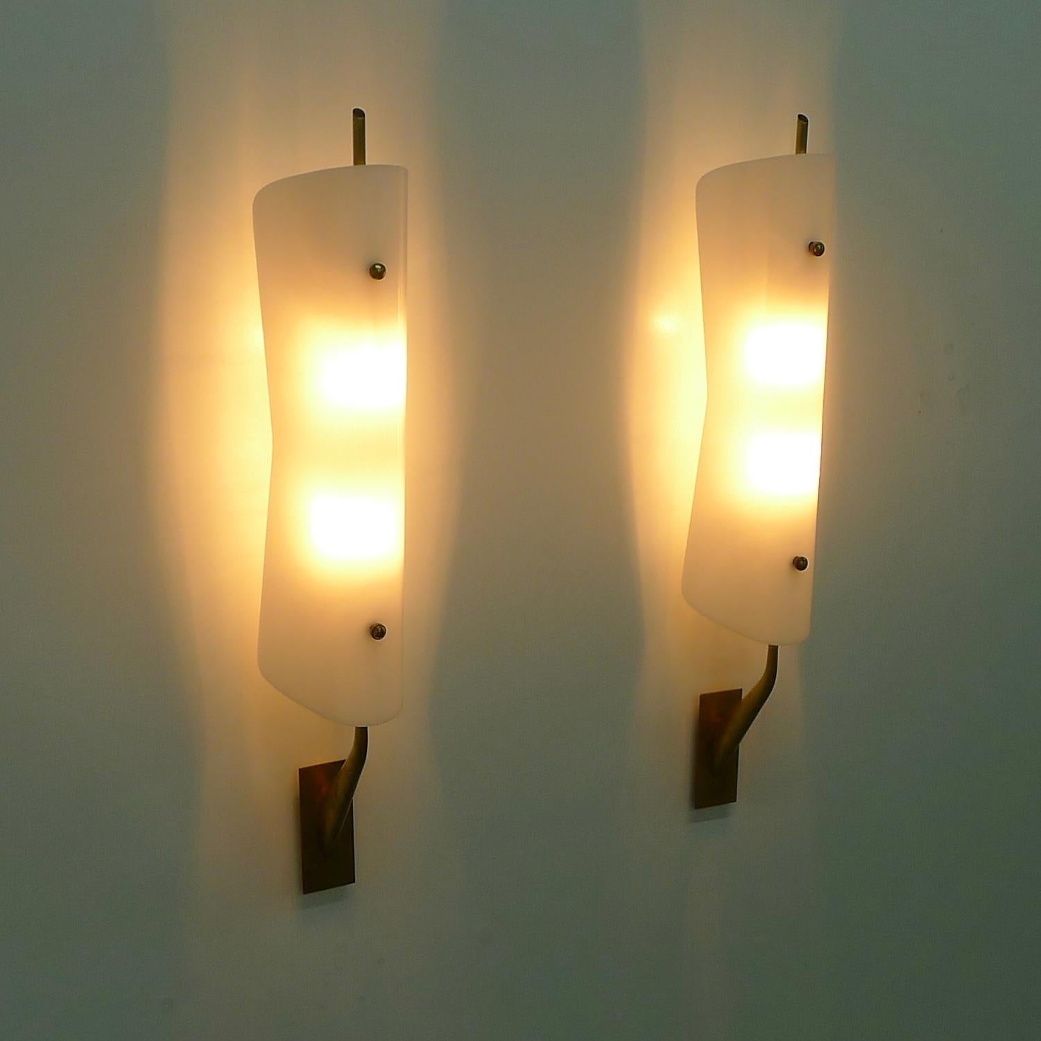 Pair of 1950s wall appliques, believed to be by Stilnovo, Italy.

Each comprises an opaque white acrylic shade of attractive waisted form which diffuses the light from two bulbs on a brass stem.  

Overall size of each 70cm high, 13cm wide, 15cm