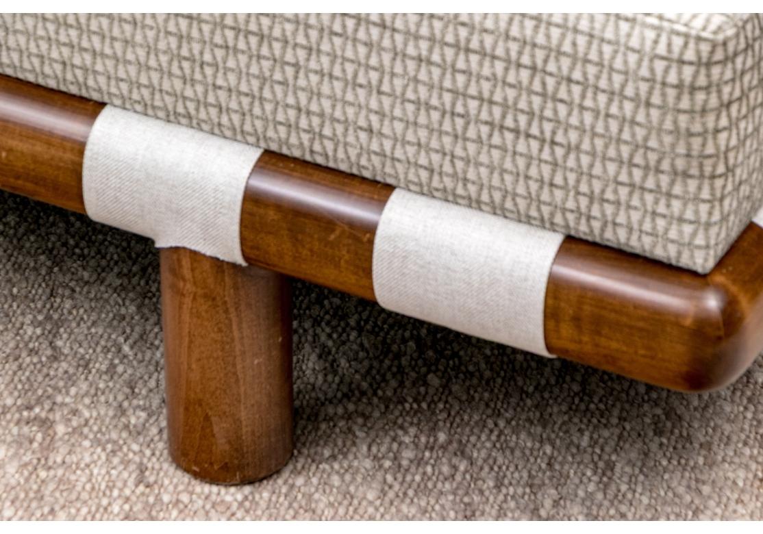 The sofa,  likely  by T.H. Robsjohn-Gibbings features a distinctive dark walnut sculpted frame with woven cotton webbing details which are hallmarks of Robsjohn-Gibbings's designs for Widdicomb. The sofa raised up on large cylindrical legs. The sofa