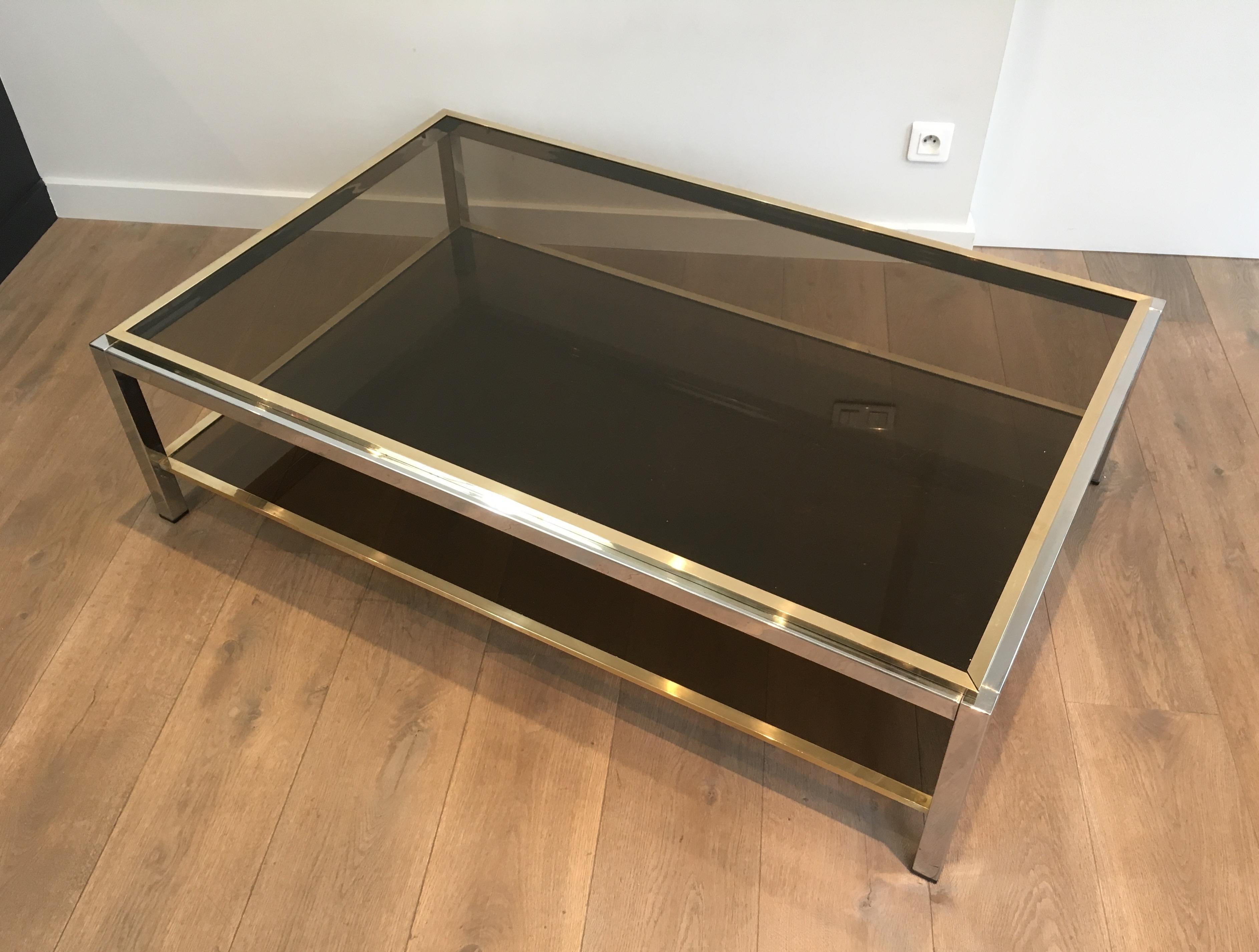 This beautiful large coffee table is made of chrome and brass with bronzed glass shelves. The top and bottom glass shelves are inserted in a brass frame constituted of 4 elements. The quality of this coffee table is very good. This is a model