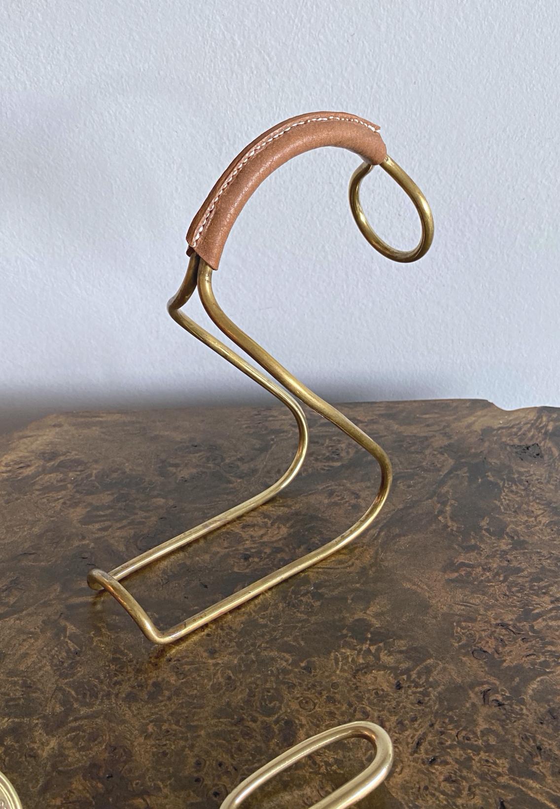 Minimalistic Auböck white or rosé wine bottle holder in solid brass with leather handle, made by Werkstätten Carl Auböck in 1950s. This pourer was designed to hold the bottle of wine in a way that helps wine aerate and the sediment settle. Nice