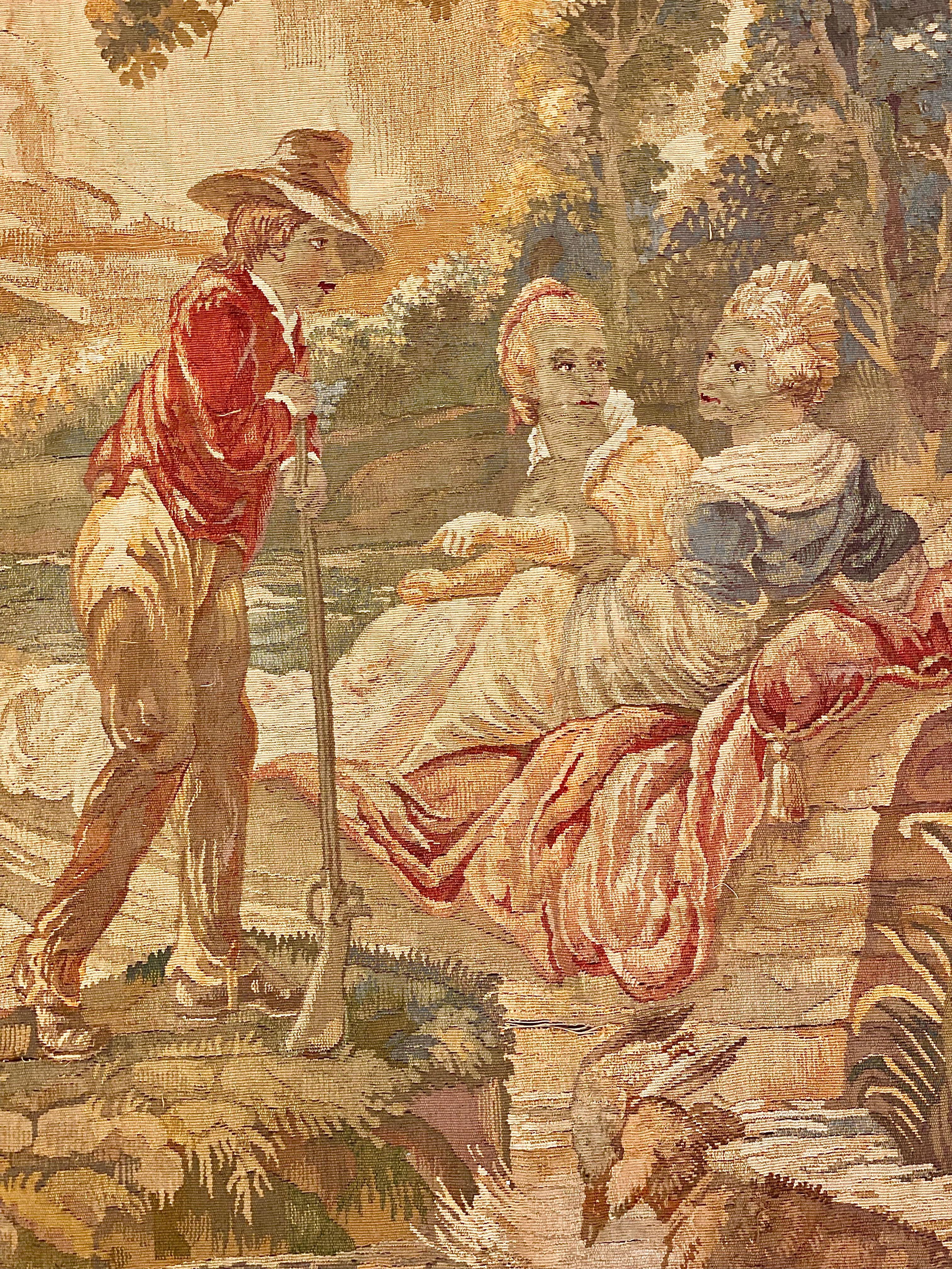 A fine and exuberant late 19th century Aubusson tapestry, depicting a gallant scene in a pastoral setting. Two maidens recline in a small boat on a river, against a background of trees and rocky outcrops in the distance. A young man pays his