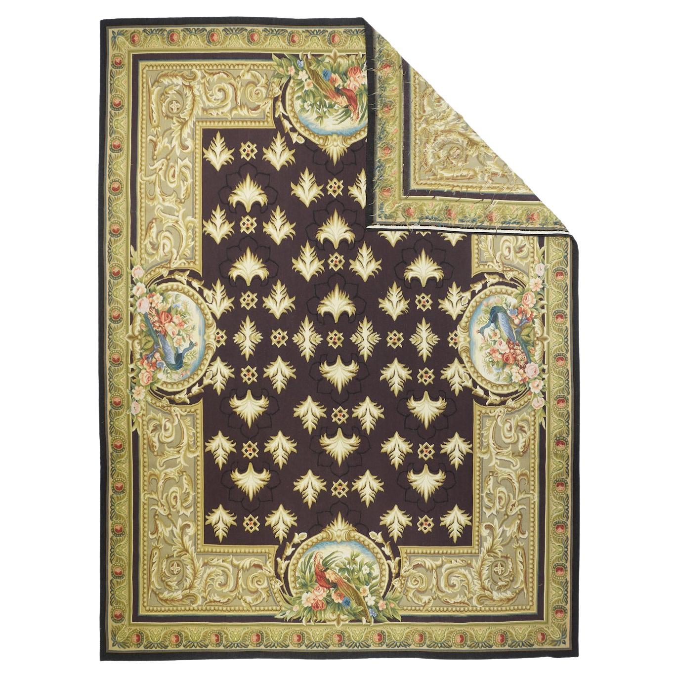 Aubusson Rug 7'11'' x 10'3''. In a sort of Louis XIV style, this tapestry weave, pileless recent piece shows a near black field with up and down feathery carnations. The trompe-l-oeil acanthus scroll main border shows cartouches with exotic birds