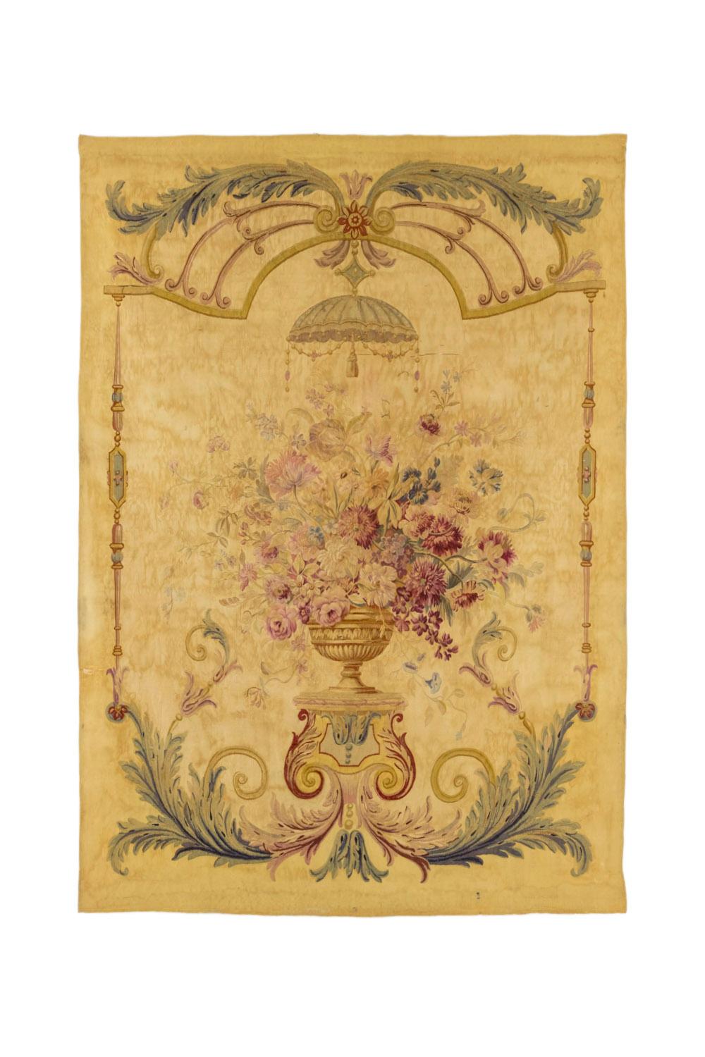 Aubusson tapestry decorated with a piedouche vase adorned with flowers and gadroons. It receives a large flowers bouquet in pink, yellow and blue tones such as peonies, forget-me-not, volubilis, etc. It stands on a piedestal that extends on the