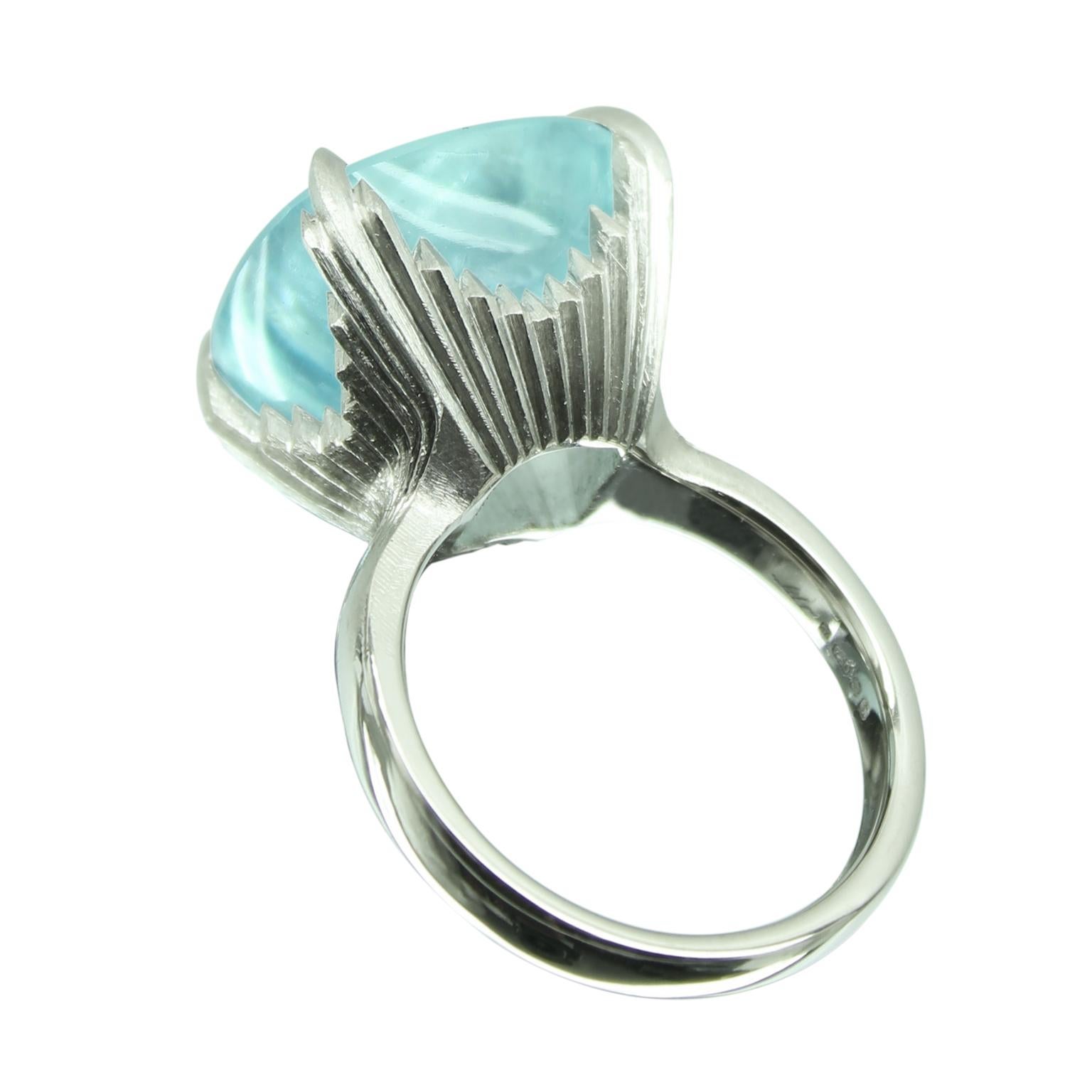 A stunning one-off 16 ct buff top cushion cut deep aquamarine stone, set into a four claw 18ct white gold ring.

The detail carries on underneath to create a raised mount of grooves and filed angles. This really catches the light as you move the