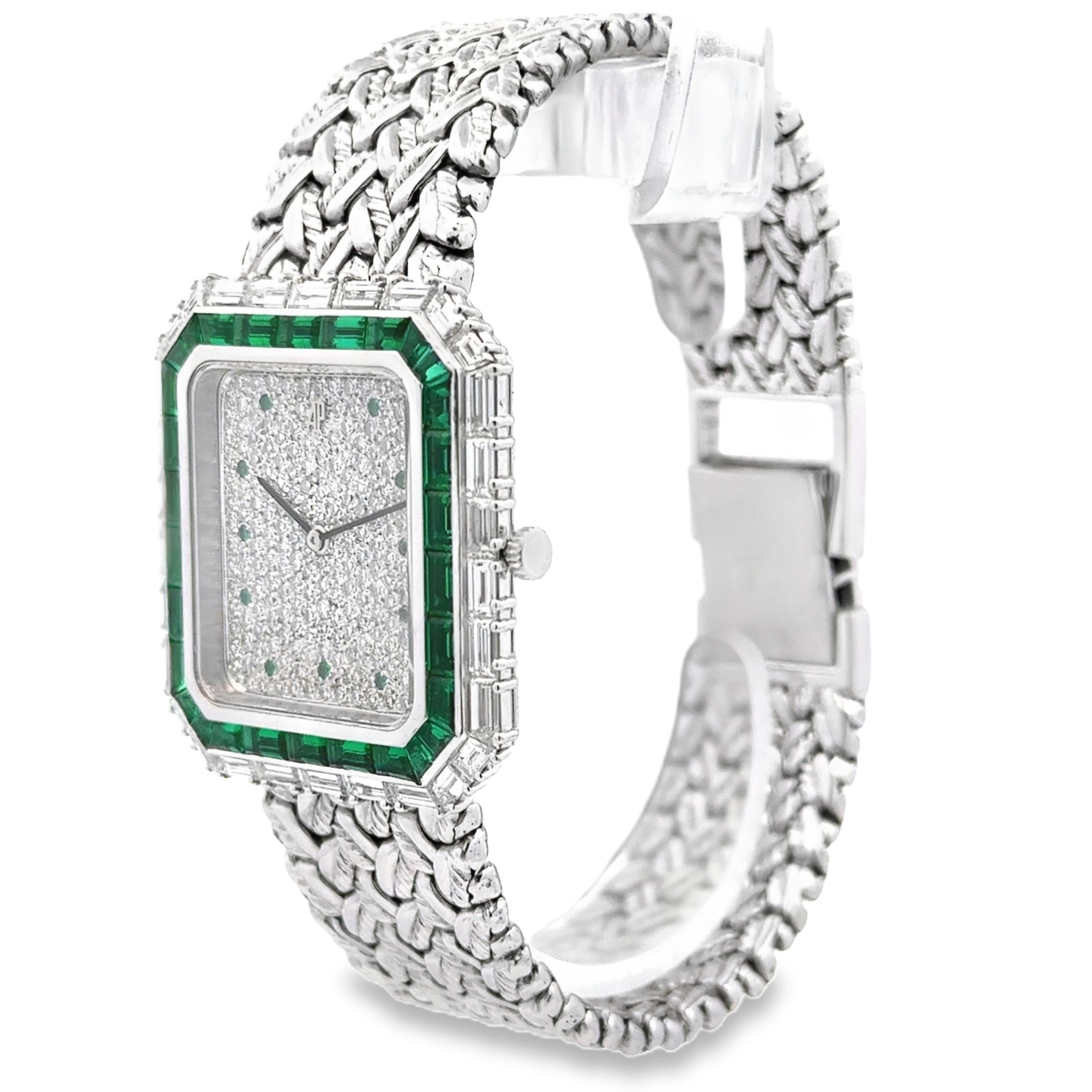 A stunning watch created by Audemars Piguet, featuring a diamond encrusted dial with hours indicated by round cut emeralds. Accented by a double halo of baguette cut diamonds and emeralds with a bracelet featuring an intricately woven