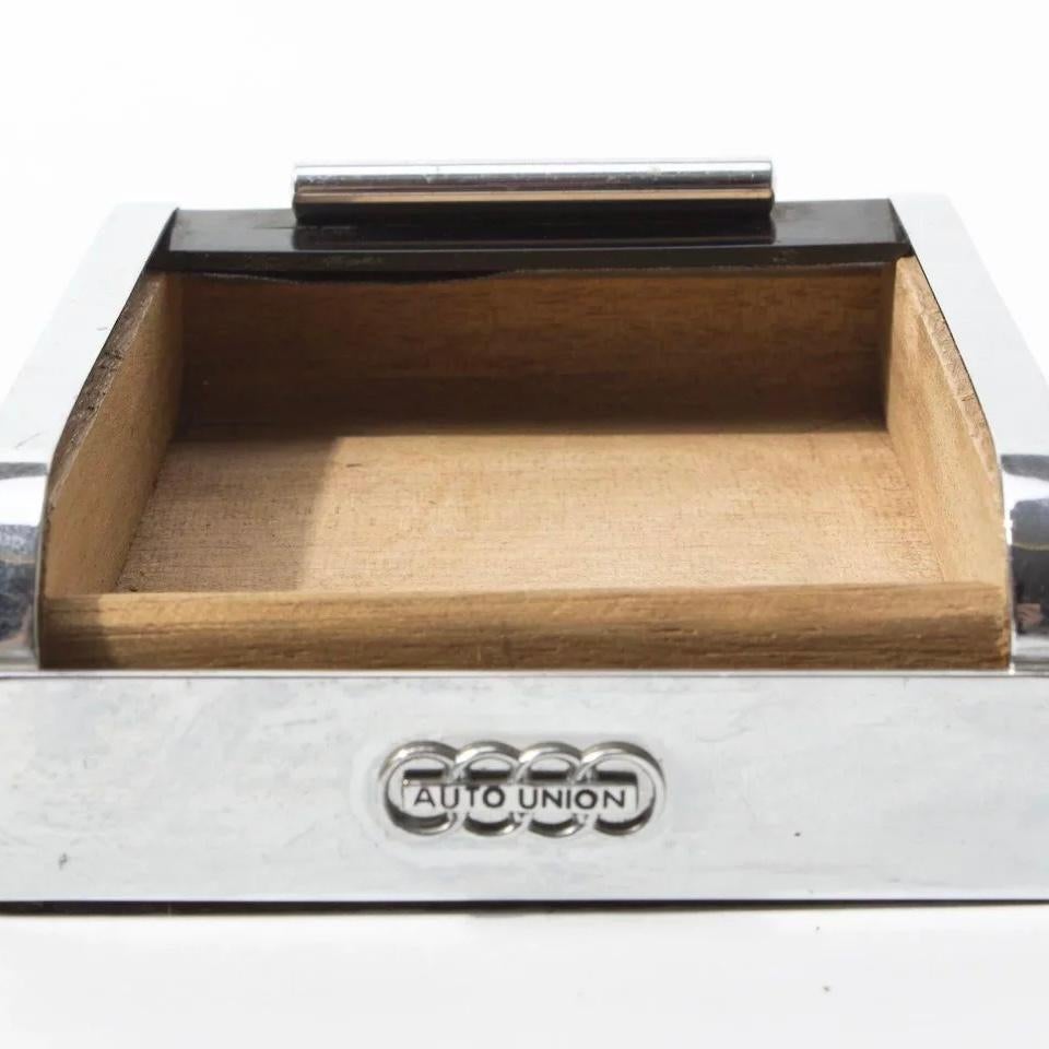 The presented rolltop dispenser was a merchandise gift designed and produced by Carl Auböck for Audi (Autounion) in the 1950s.

Made from the typical chrome plated brass, a lacquered roll top lid an rosewood.

A similar dispenser is illustrated