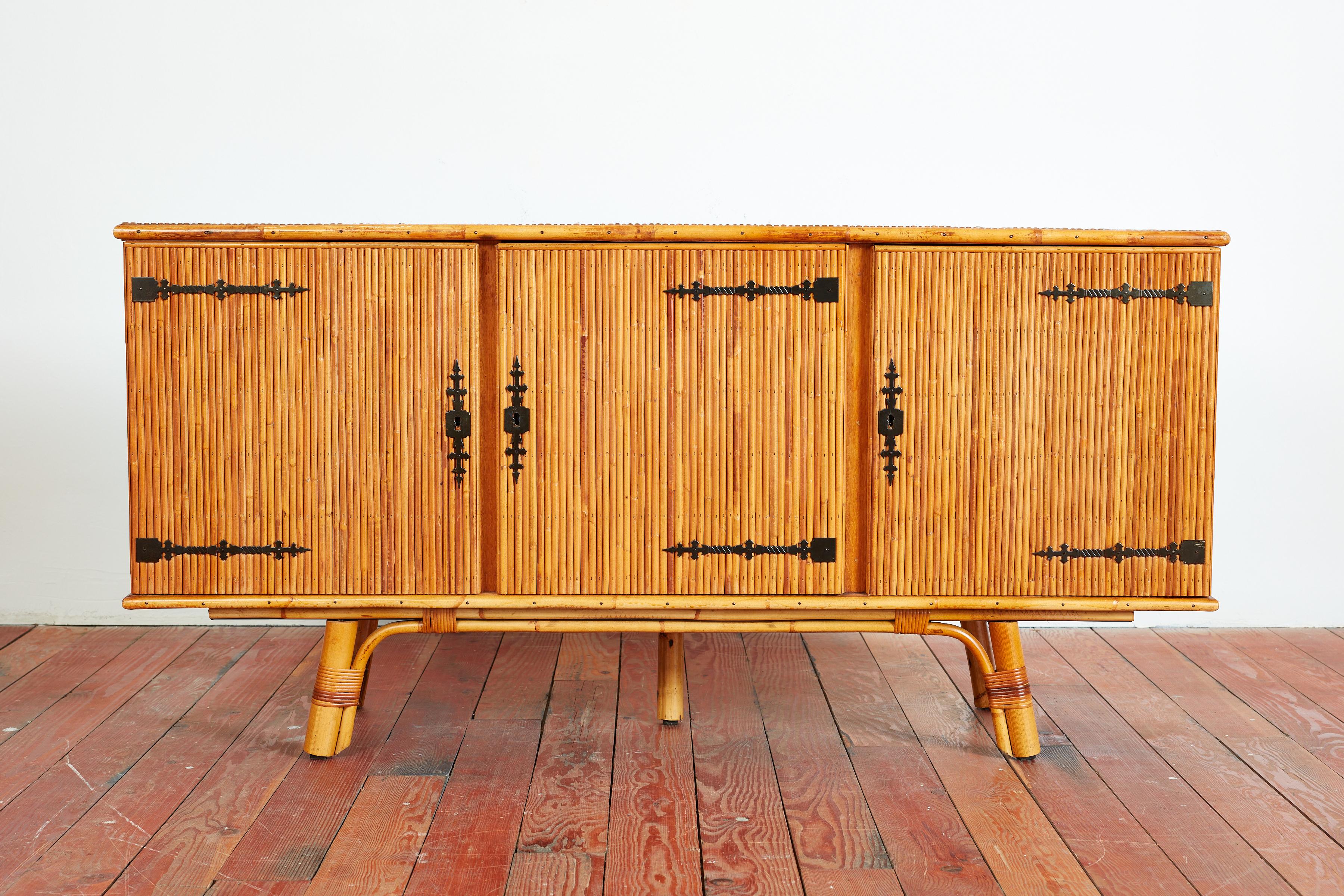 Beautiful split bamboo sideboard by Adrien Audoux and Frida Minet
France, 1950s.
Three-door cabinet with intricate wrought iron hinges, interior shelves for storage  and original key. 
Bamboo legs with rattan wrapped detail.
Wonderful patina