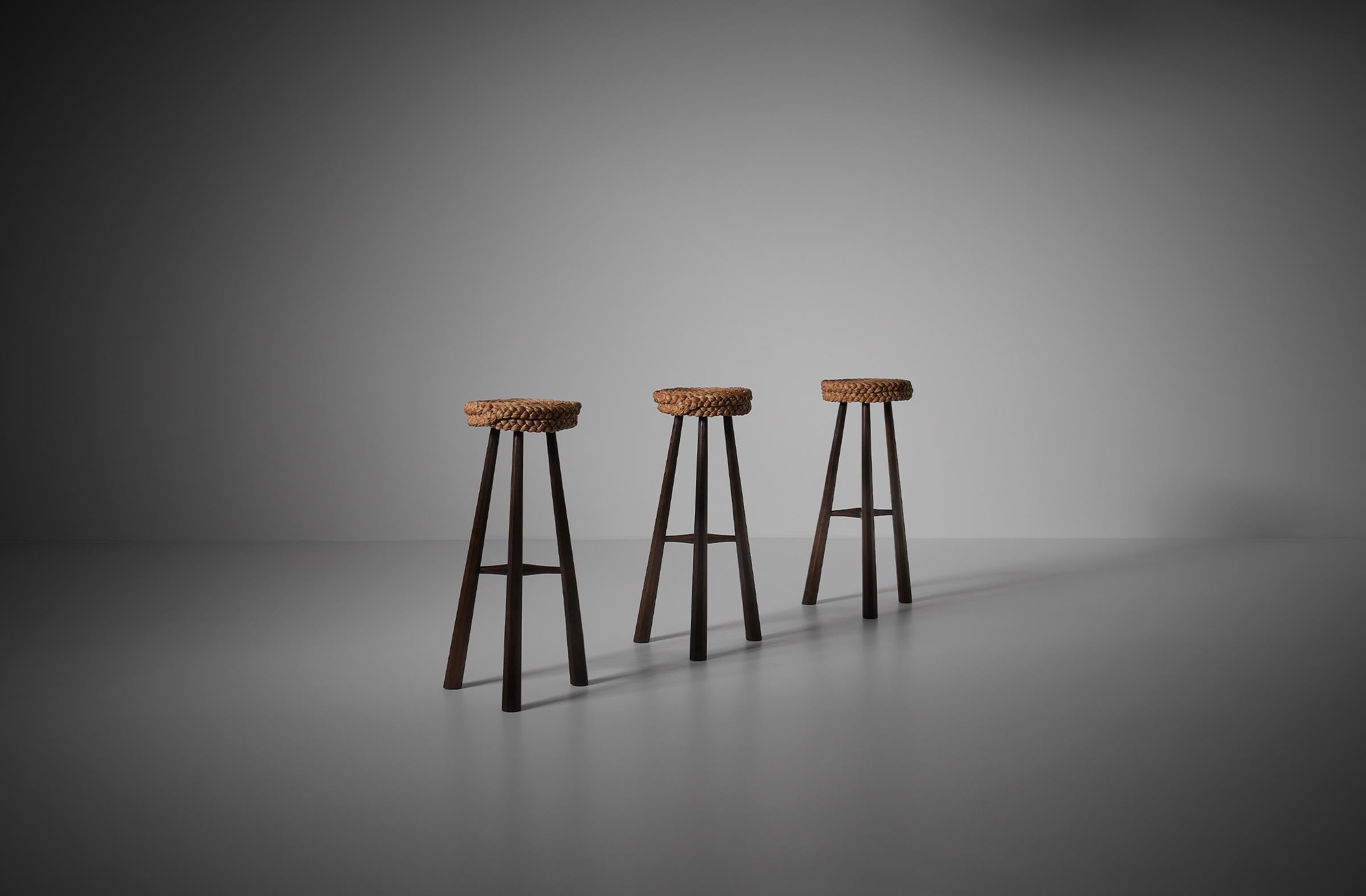 Set of three Audoux & Minet bar stools, France 1950s. The stools are constructed out of dark stained Ash wood which contrasts beautifully with the refined fresh rope seats. The carving and position of the legs gives the stools a nice and playful