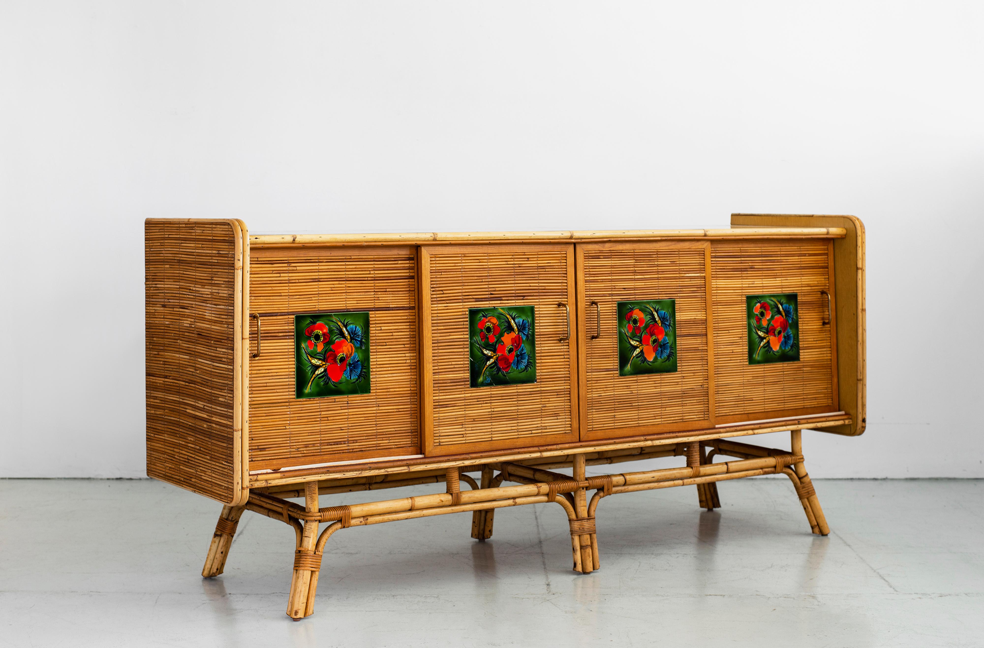 Beautiful French rattan sideboard by Adrien Audoux and Frida Minet, circa 1960s. Made of rattan wood on sides and front with floating rattan base and laminate wood top. Rattan sliding doors have hand painted floral ceramic tile detail which open to