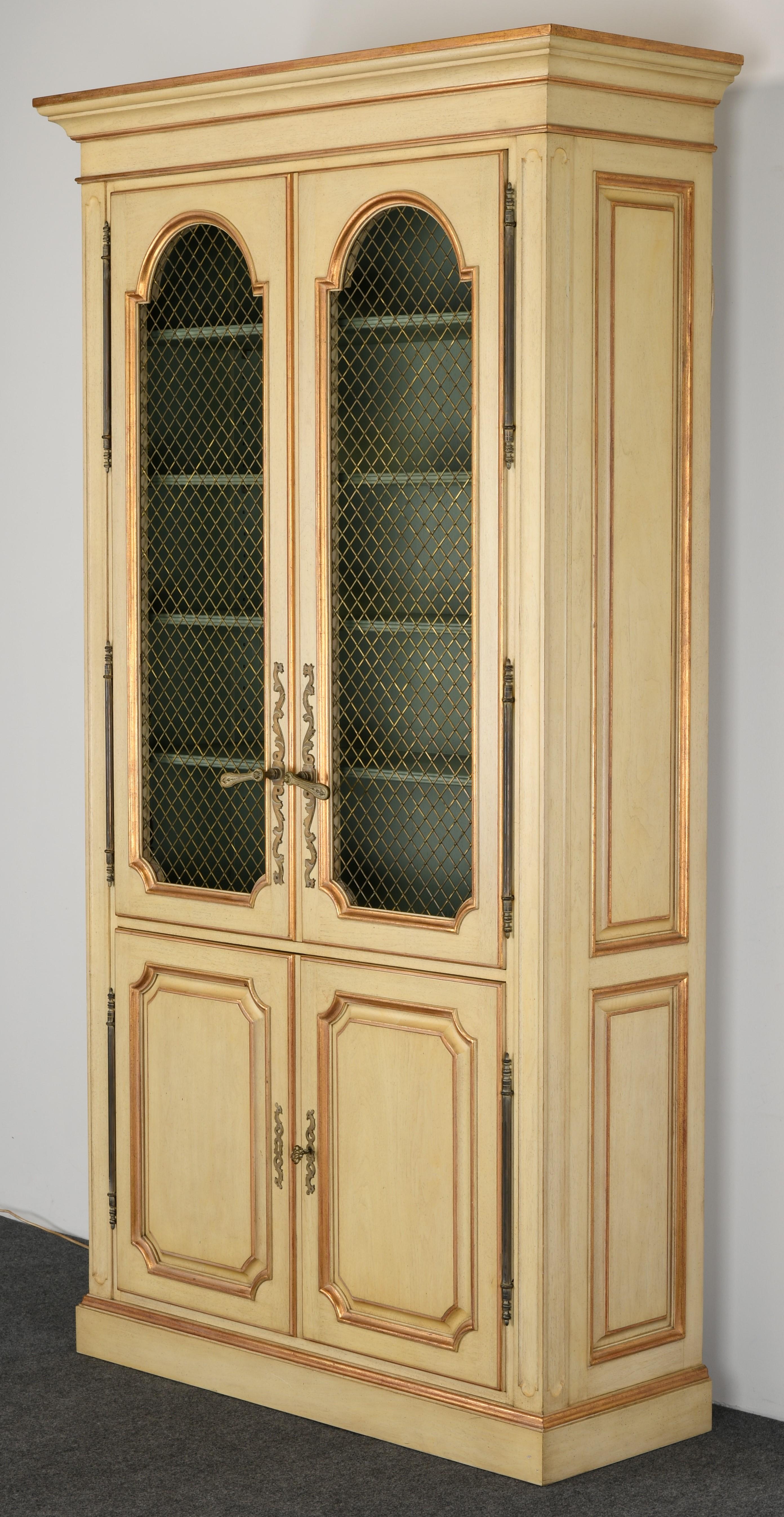 A stately French Provincial or country French display cabinet. This vitrine has decorative arched windows with bronze mesh wire fronts. The cabinet has seven shelves, five of which are painted a beautiful sage green. This display case lights up as