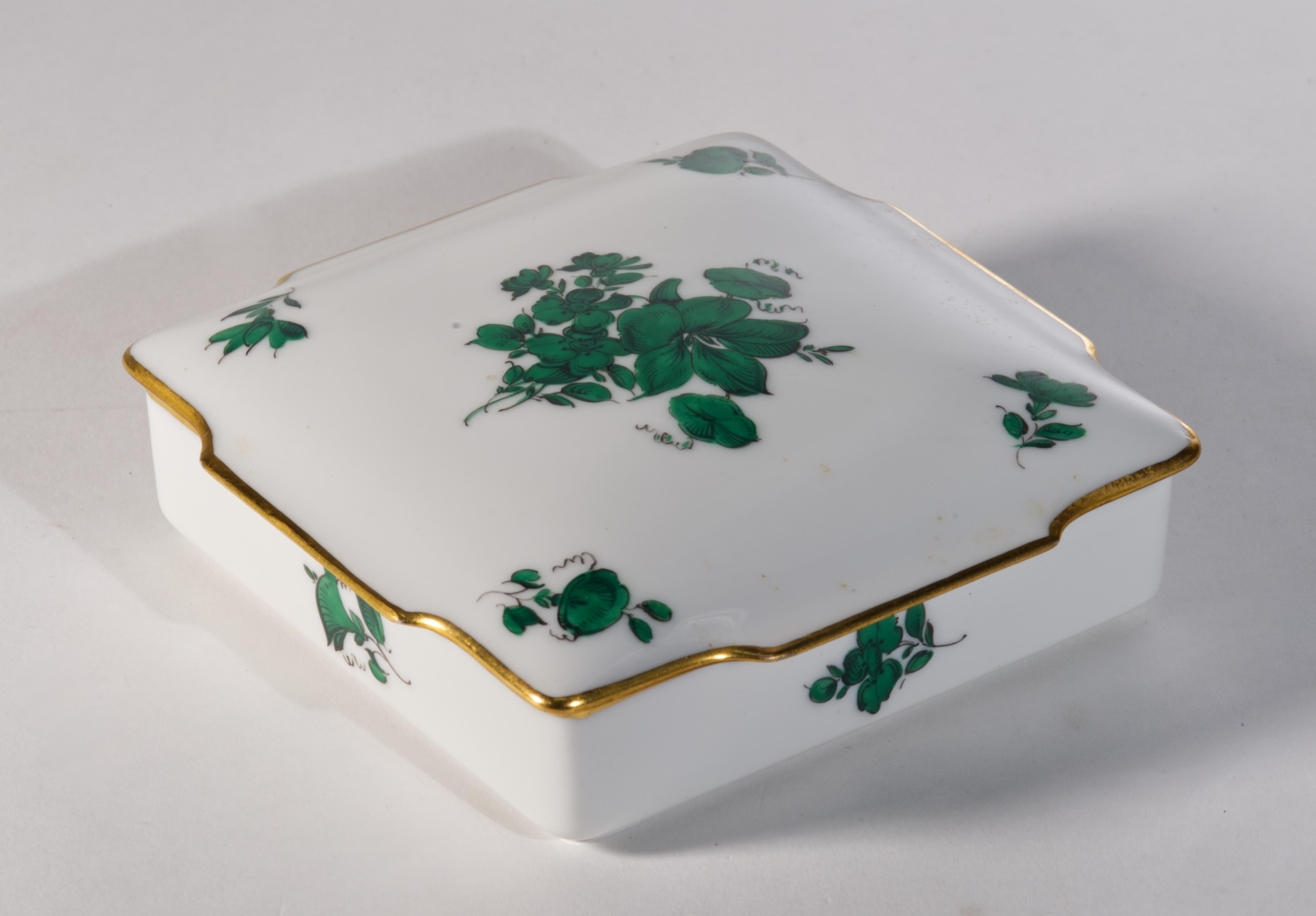 Cette boîte à vêtements ou à bijoux en porcelaine d'époque présente une forme carrée avec un couvercle sculptural, inspiré des boîtes anciennes de style Biedermeier, avec un décor floral vert foncé avec un contour noir et des bordures dorées sur la