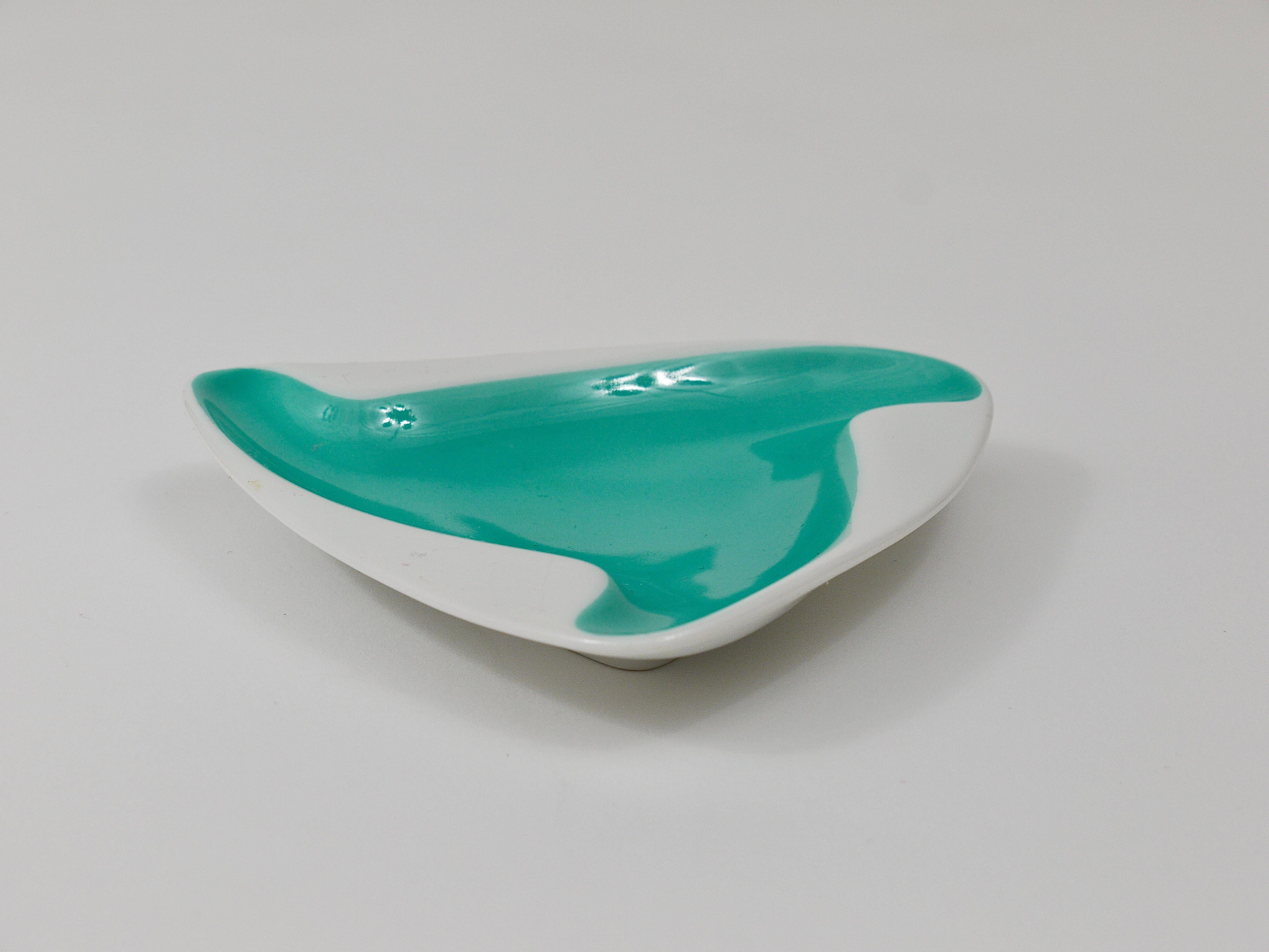 Un pequeño cenicero triangular modernista muy encantador de la década de 1950. Fabricada en porcelana con un esmalte brillante de color turquesa pastel y blanco. Una pieza preciosa, ejecutada por Augarten Viena, Austria. En muy buen estado.