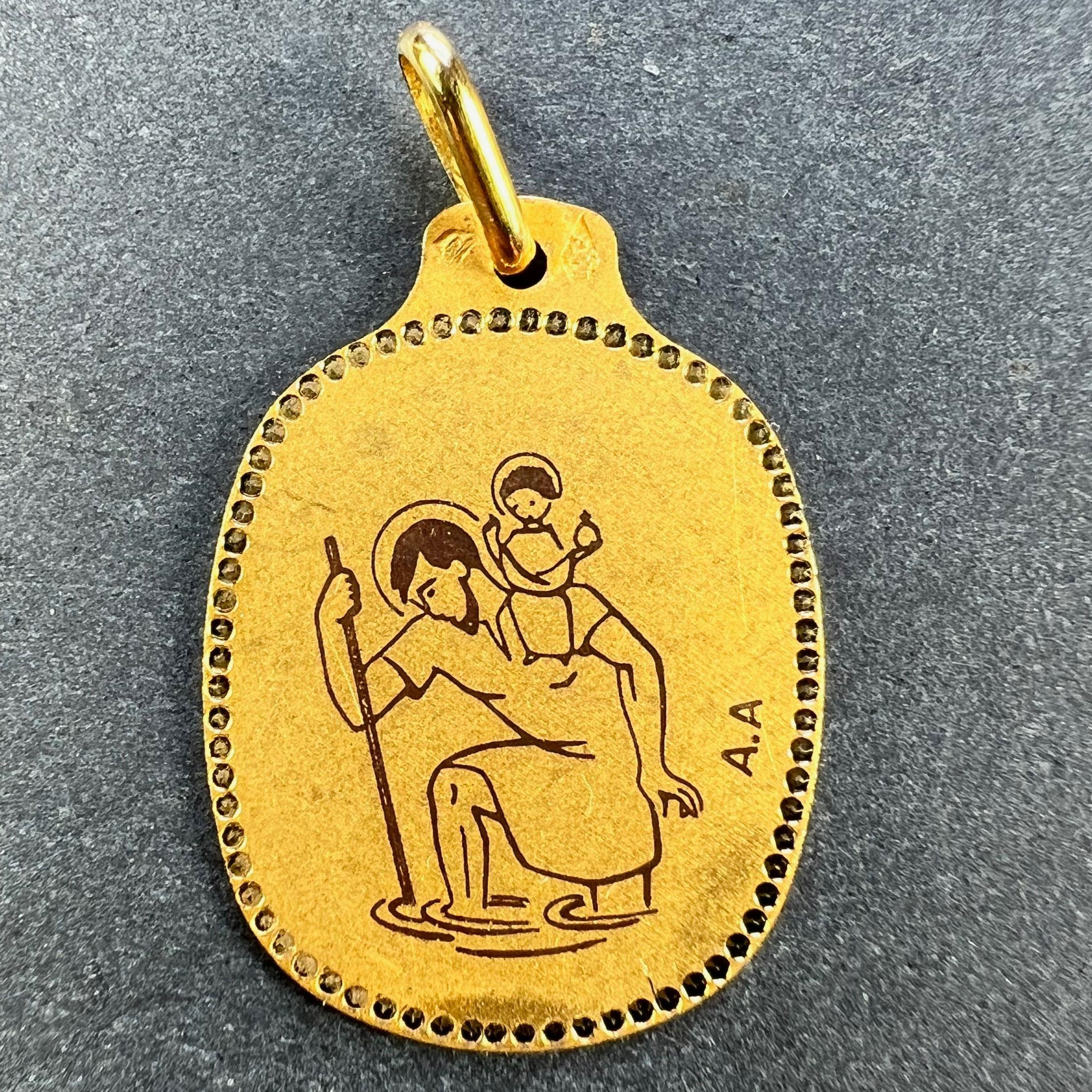 A French 18 karat (18K) yellow gold charm pendant or medal by Augis depicting St Christopher carrying the infant Christ across the river with black enamel detail and punched dot border. Stamped with the eagle's head for French manufacture, Augis'