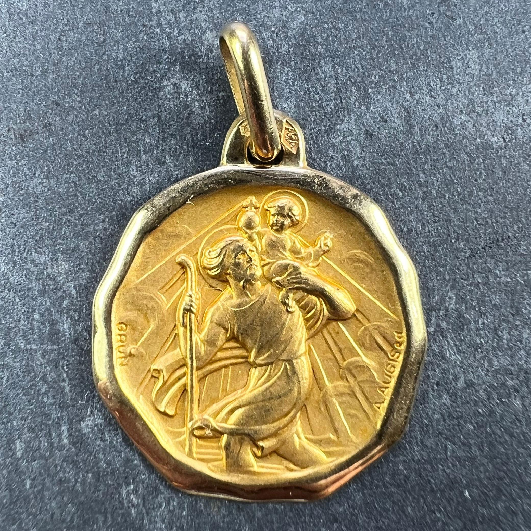 A French 18 karat (18K) yellow gold charm pendant or medal designed by Grun for Augis depicting St Christopher carrying the infant Christ across the river. Stamped with the eagle's head for French manufacture, Augis' makers mark, and signed A. Augis