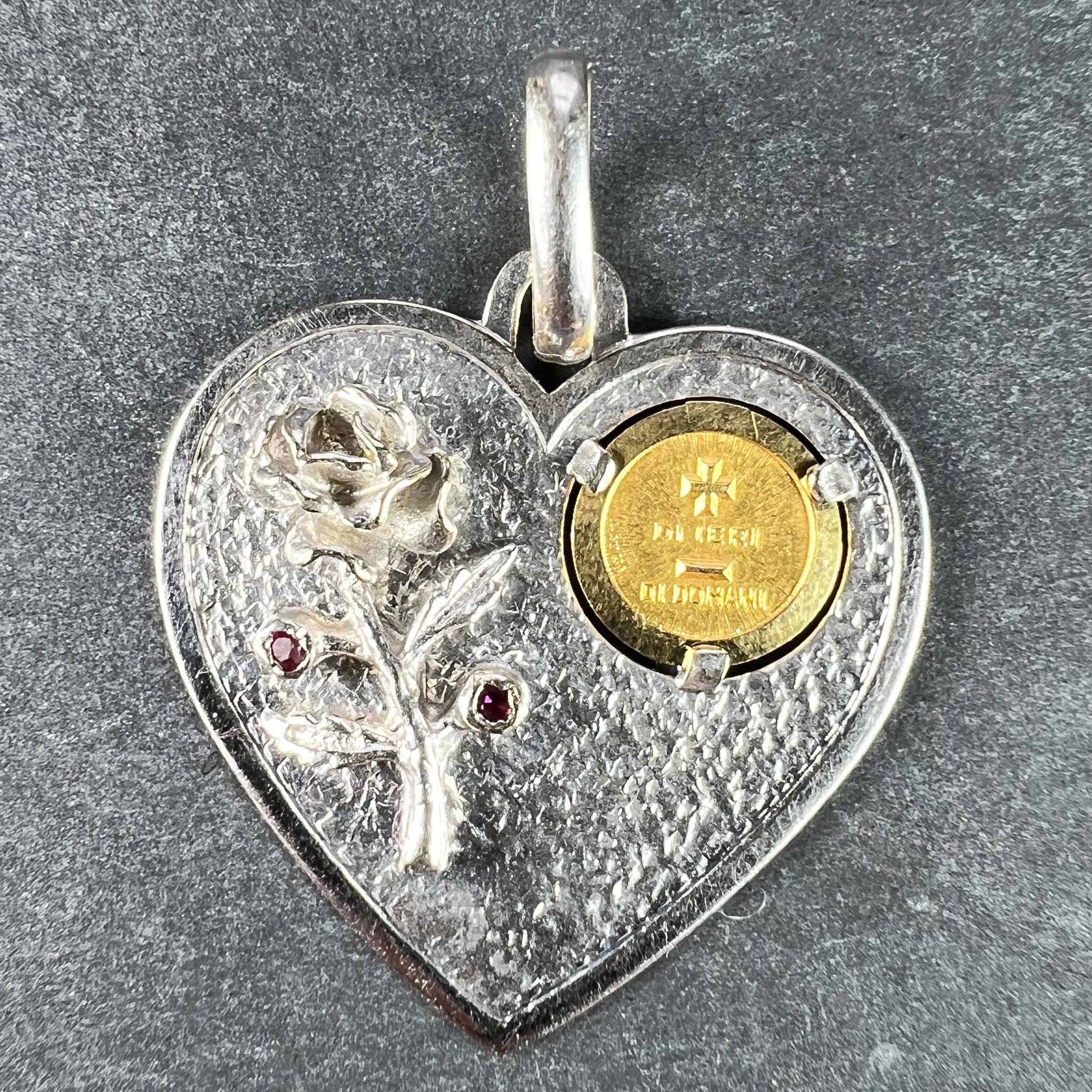 An Italian 18 karat (18K) white and yellow gold love charm pendant designed as a white gold heart with a sculpted rose set with two ruby flower buds. To the right-hand side an inset yellow gold medallion with a rebus spelling out 
