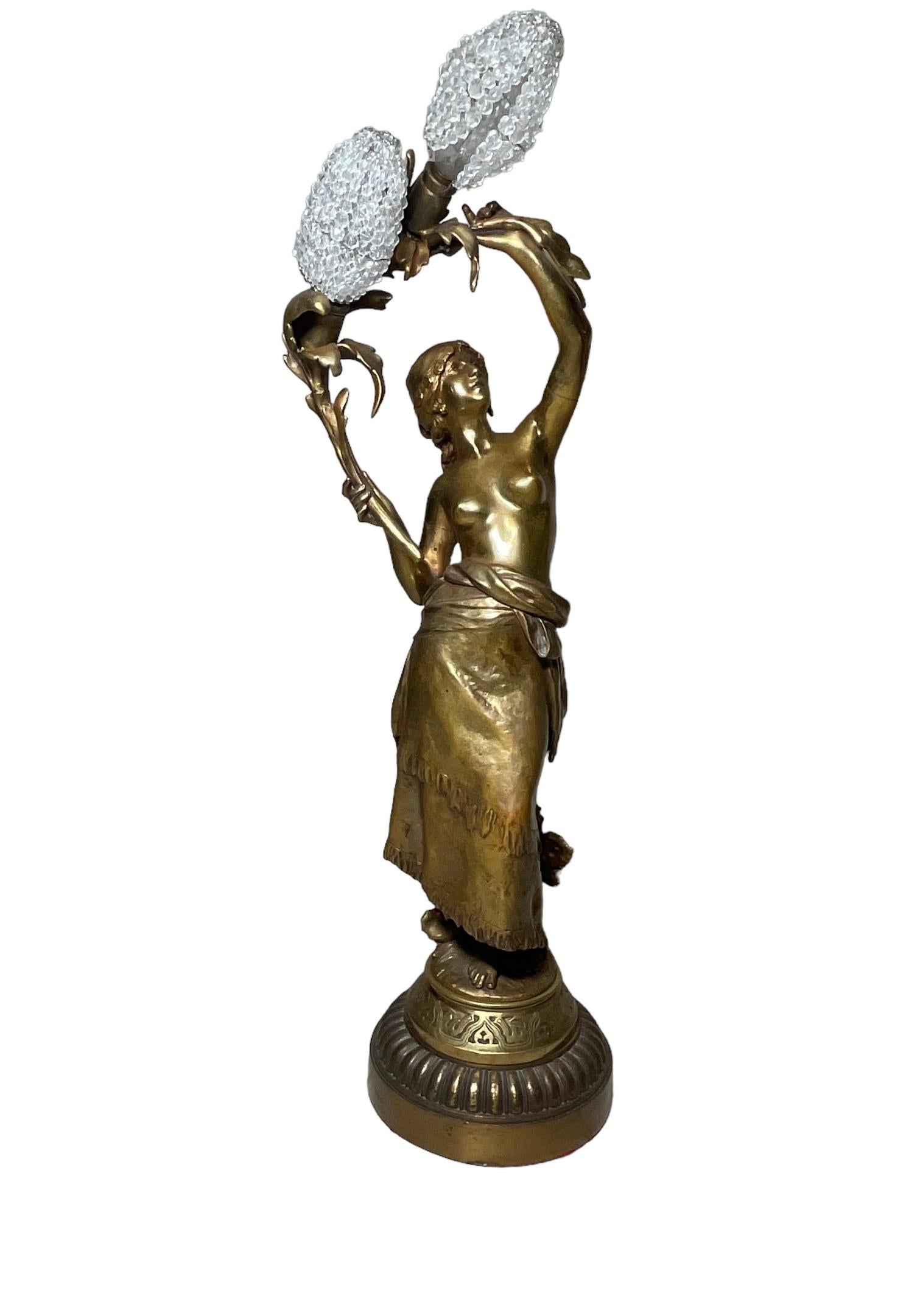 This is an Auguste Moreau bronze sculpture of a gypsy lamp. It depicts a naked upper chest young lady and barefoot in the grass who is holding up a long branch of leaves forming an arc. She is wearing a head wrap and a long Wraparound fringed skirt.