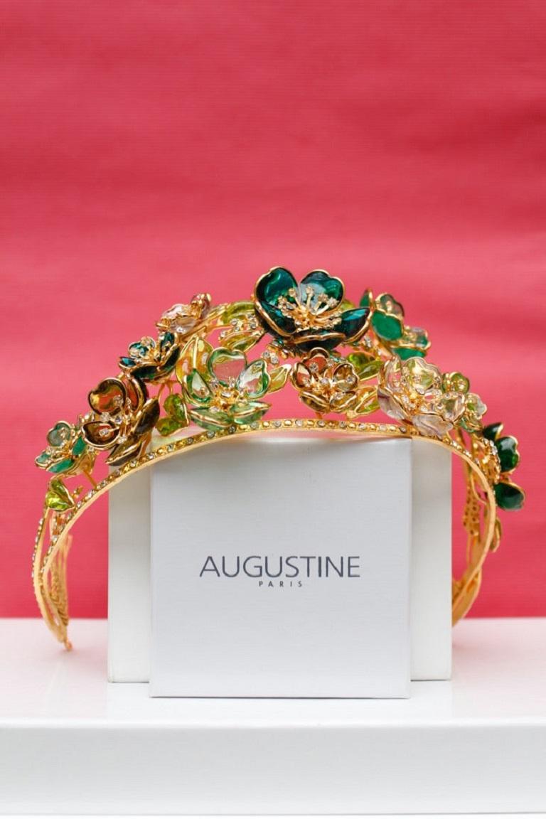 Augustine (Made in France) Tiara aus vergoldetem Metall, Glaspaste und Strasssteinen.
 Er wird mittels kleiner vergoldeter Metallzähne befestigt und kann in beide Richtungen getragen werden. Auf der Rückseite signiert. 
Es handelt sich um ein