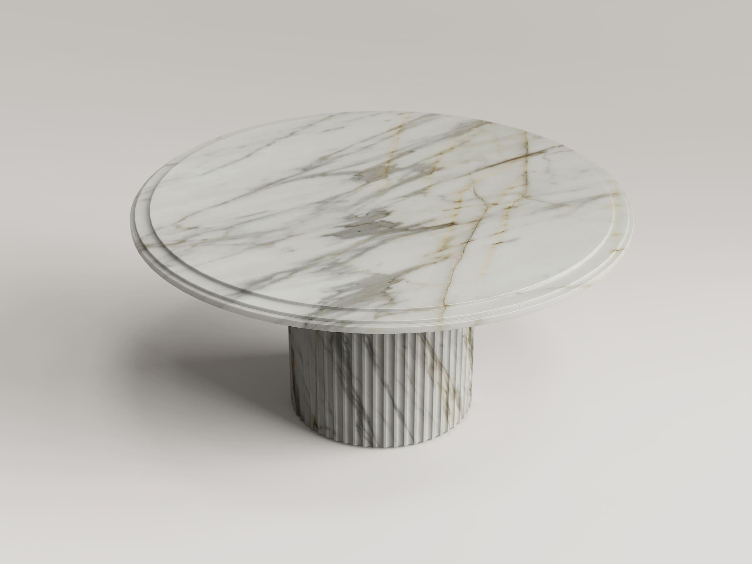 Une table sculpturale, entièrement réalisée en marbre Calacatta de première qualité, symbole de luxe et d'élégance intemporels.
La base cylindrique présente des rainures verticales raffinées, réalisées avec une extrême précision, qui confèrent