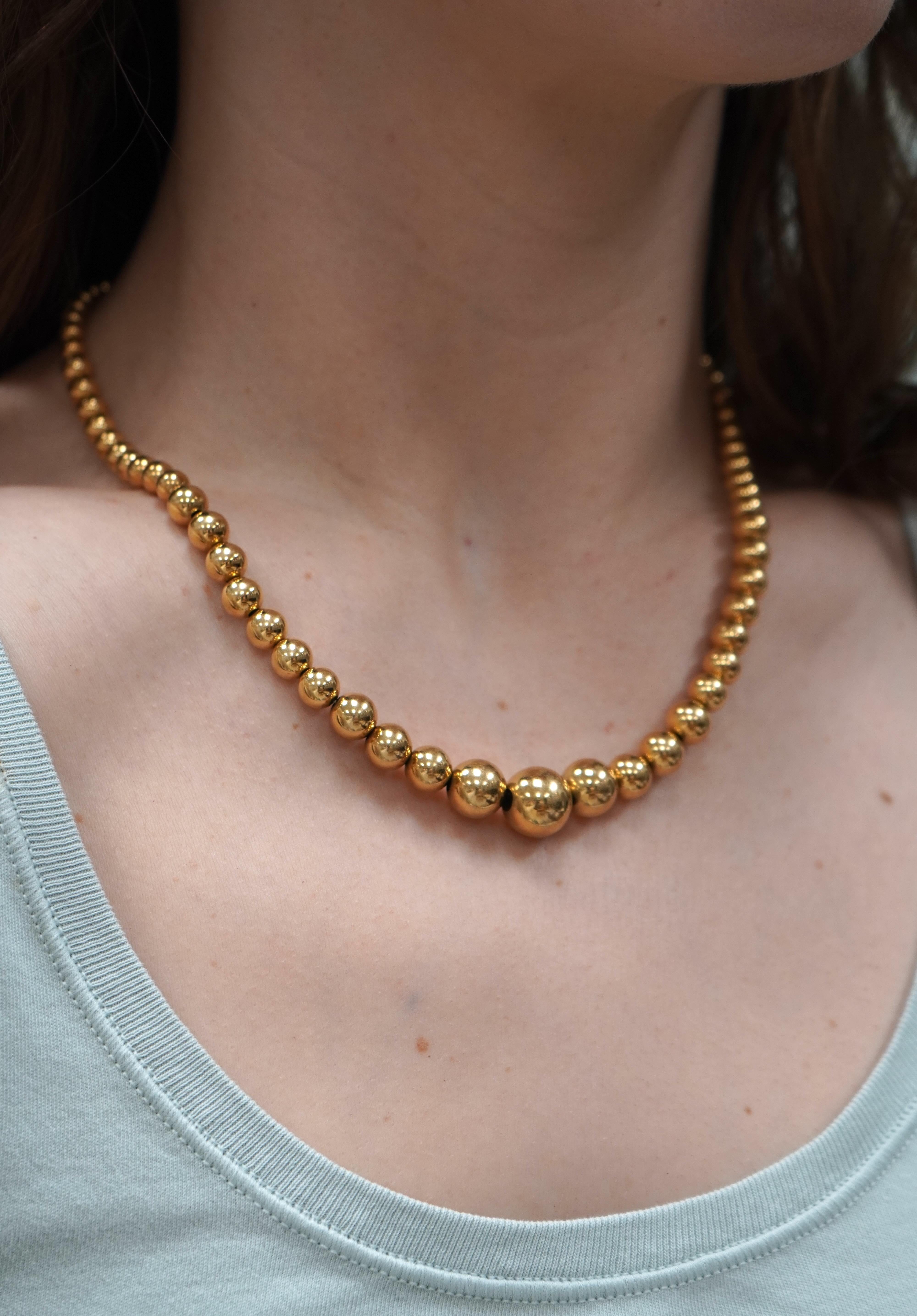 This 18k gold beaded necklace by Aurafin features a graduated design with polished, hollow beads for lightweight comfort and easy daily wear. The largest bead at the center measures 6mm, with smaller beads tapering up the neckline for a balanced and