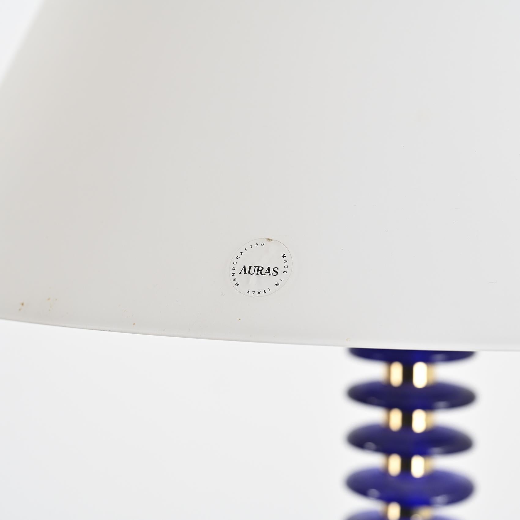 
Un lampadaire d'Auras Italia, conçu dans les années 1980.

Cette lampe se compose d'une base circulaire en métal laqué bleu foncé et d'une tige en laiton ornée de disques en verre bleu soufflé à la bouche. Le réflecteur en verre satiné en forme de