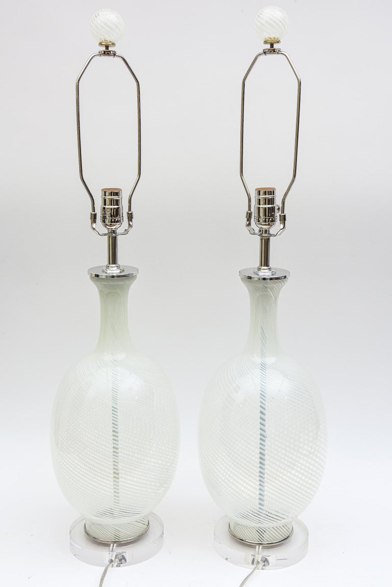 These pair of vintage Italian Murano Aureliano Toso white swirled glass lamps have chrome appointments and the original swirled glass balls as the finials. They have been rewired and cleaned. The glass finials are 2.5 inches H x 2.5 D. To the top of