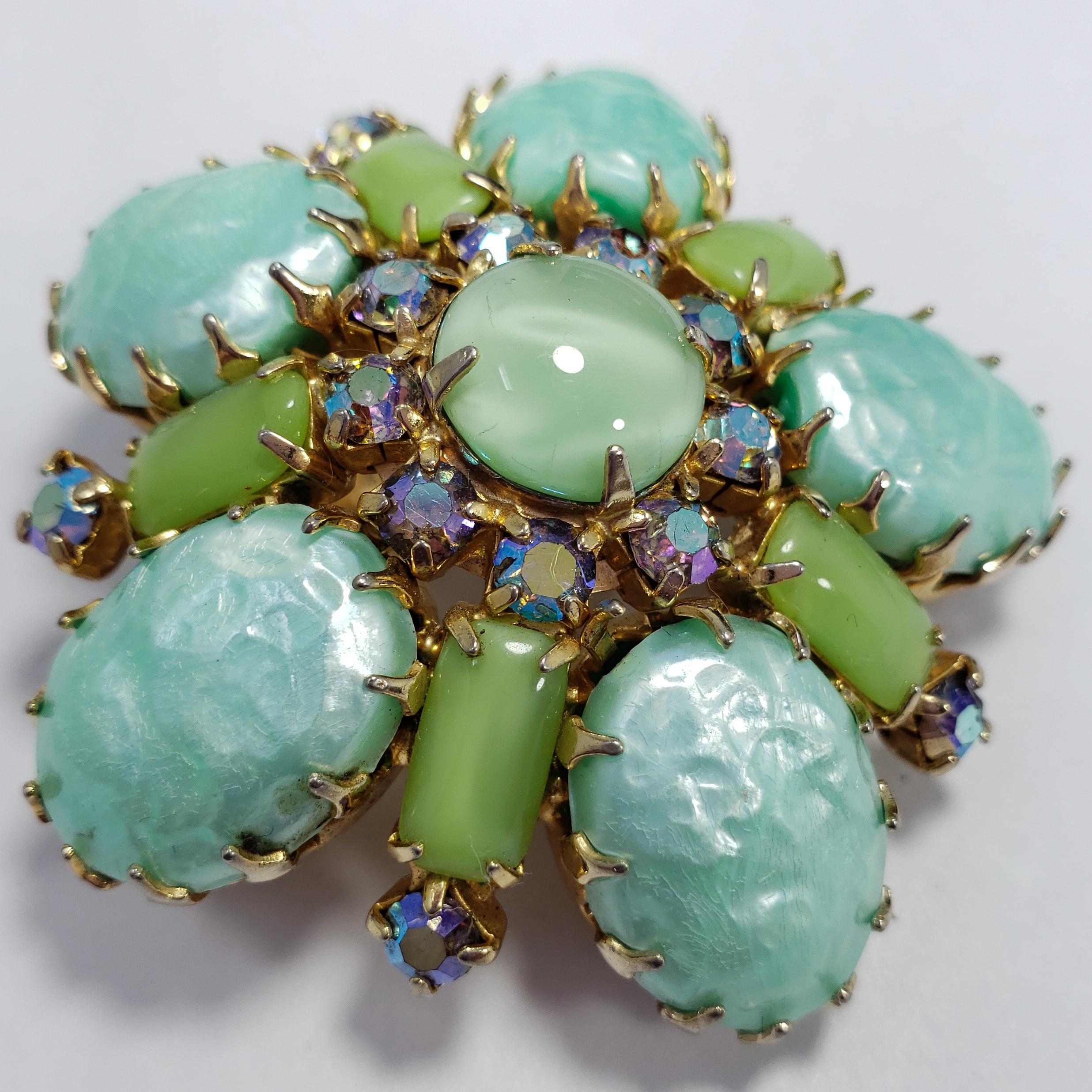 An exquisite round brooch by an unknown designer from the mid-1900s. Features prong-set cabochons in a variety of green toes, accented with sparkling aurora borealis crystals. Set in vintage gold-tone metal setting.