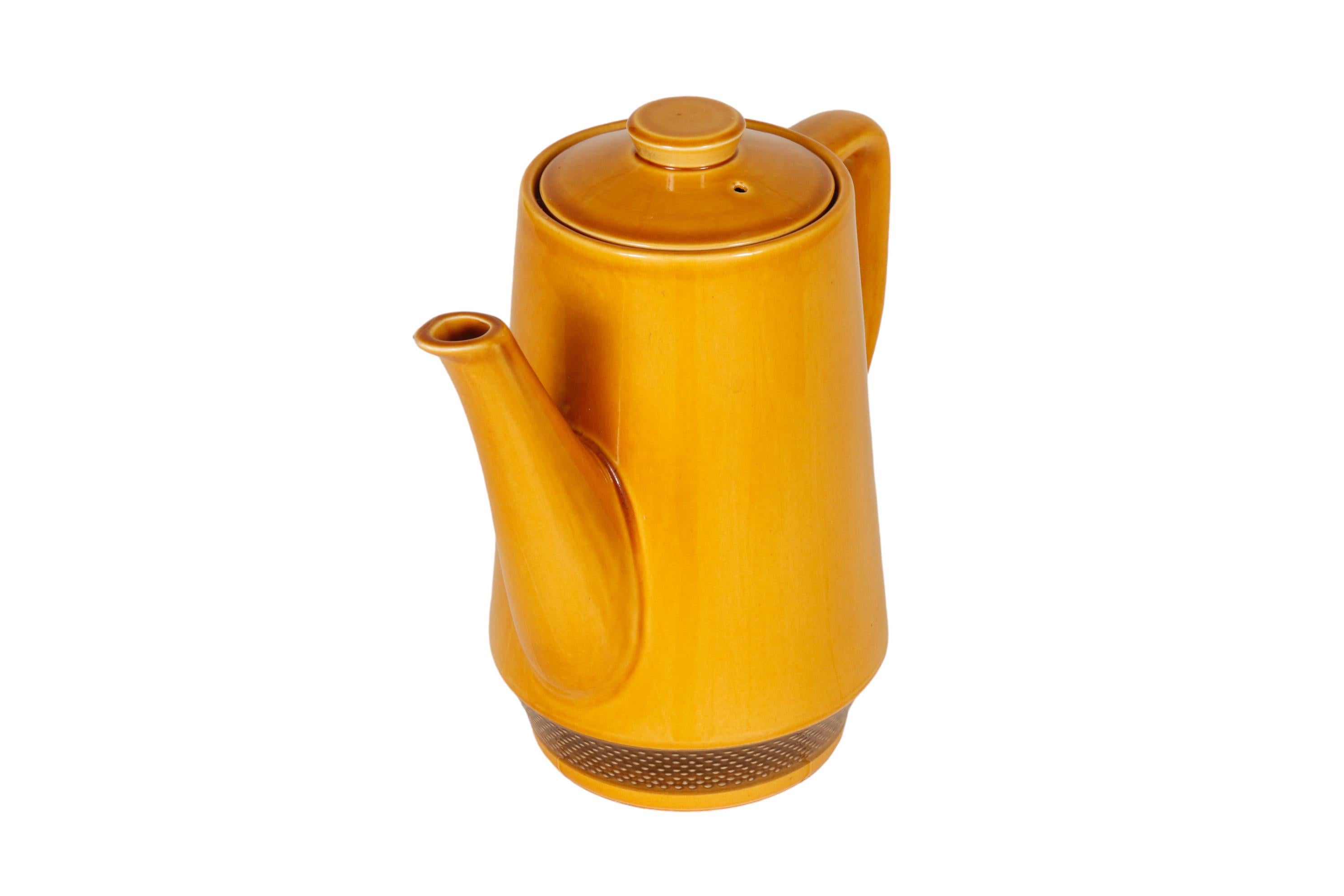 A Japanese mid-century coffee pot in mustard yellow, made by Aurora Ironstone. Sleek lines throughout, with a straight spout and squared handle. The body of the pot is decorated with a brown beaded band around the base. Marked underneath “Aurora