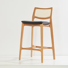 Taburete Aurora, madera maciza color miel claro, respaldo de caña natural, cuero natural negro