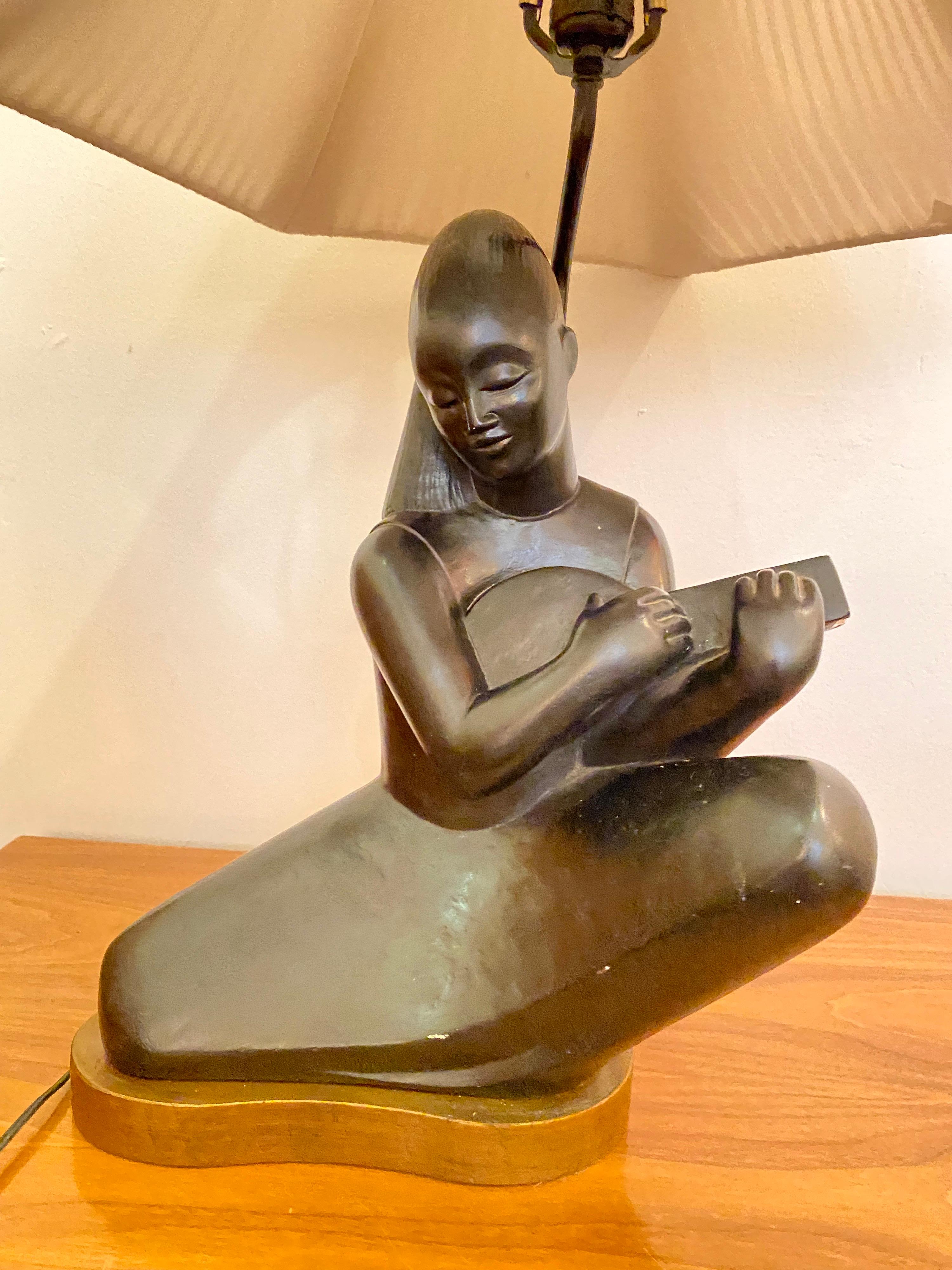 Austin Productions seated woman playing a Banjo. Finished in black sitting on a free-form wood base. String shade included. Signed at dated to back. Dates to the 1960's.