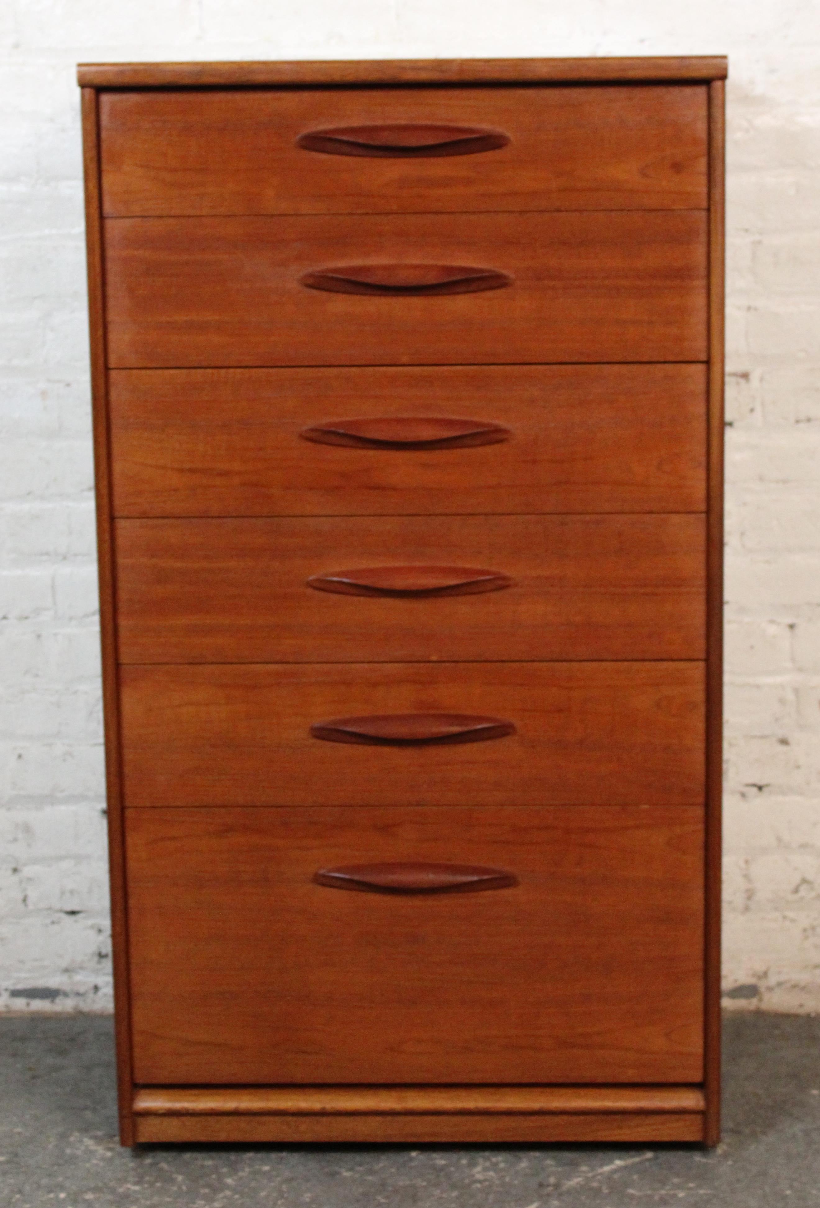 Un refinado y esbelto arcón lencero de teca del fabricante británico Austinsuite. Con seis cajones graduados con tiradores esculpidos, esta pieza muestra líneas limpias y ricas vetas de madera típicas del diseño de mediados de siglo. Perfecta para