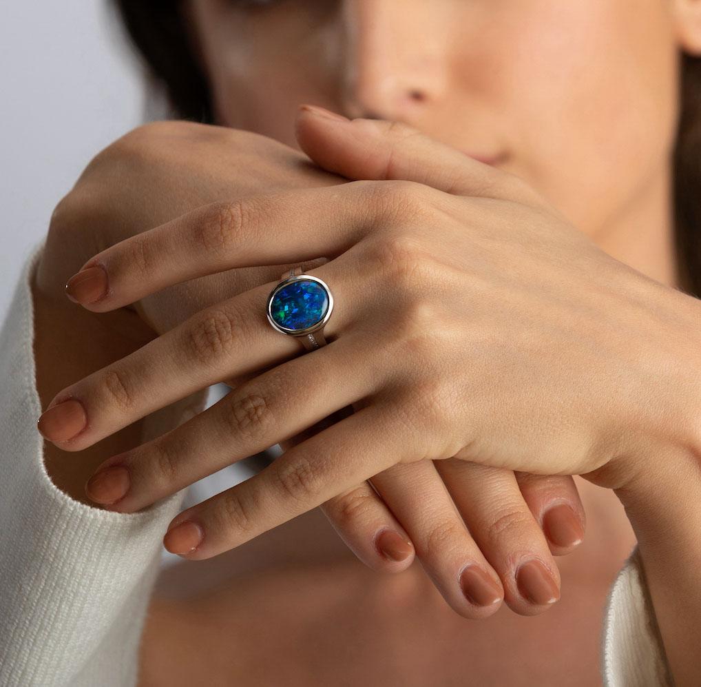 A sensual and romantic charm imbues the 'Silhouette of Desire' opal ring featuring an impressive black opal from Lightning Ridge, Australia. This sublime gemstone presents a deep blend of emerald and azure hues that captivates at one glance.