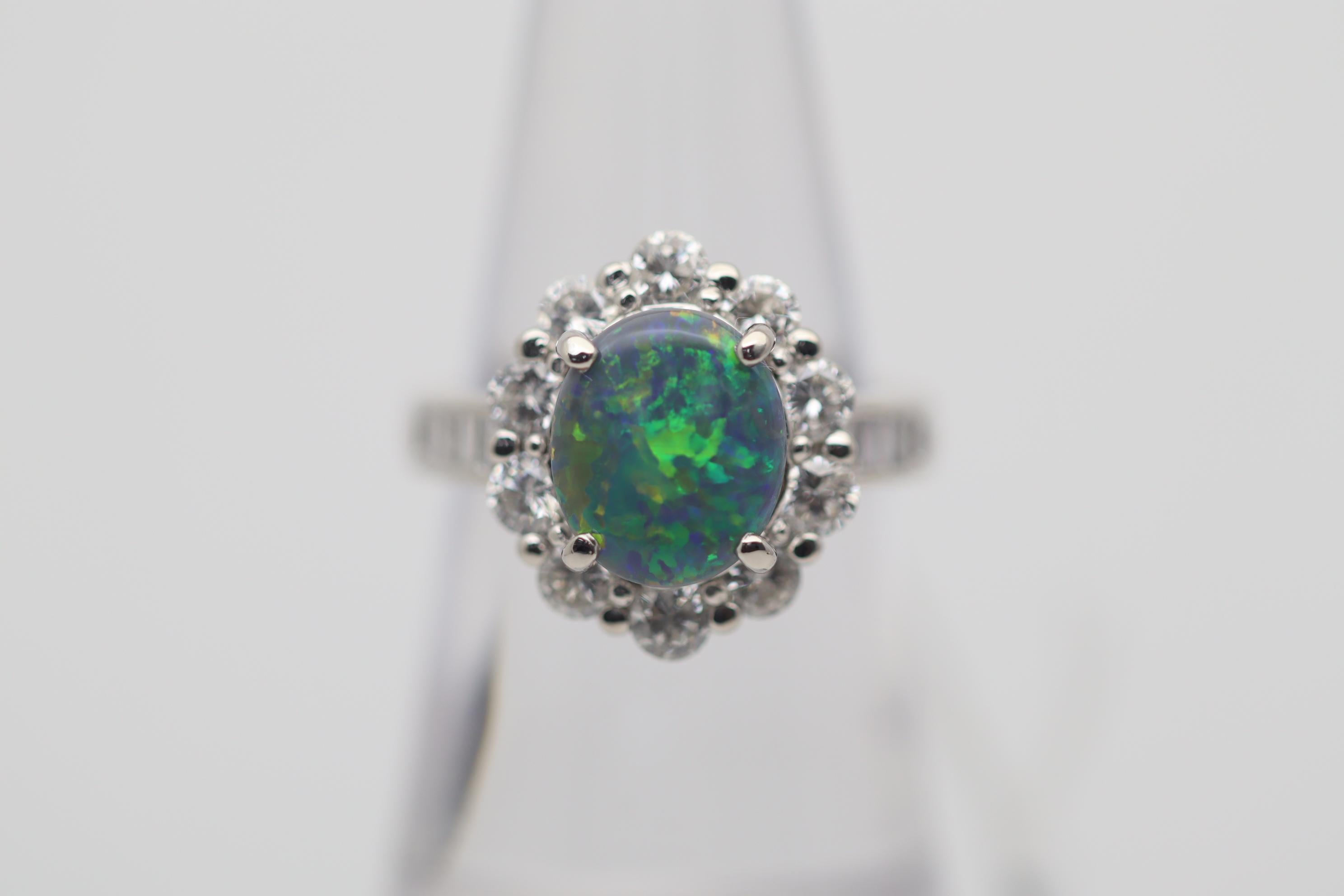 A fine natural black opal from Australia takes center stage. It weighs 1.84 carats and has great play-of-color as large bright flashes of green, orange, and yellow dance across the stone along with some blues and reds. It is complemented by 1.24