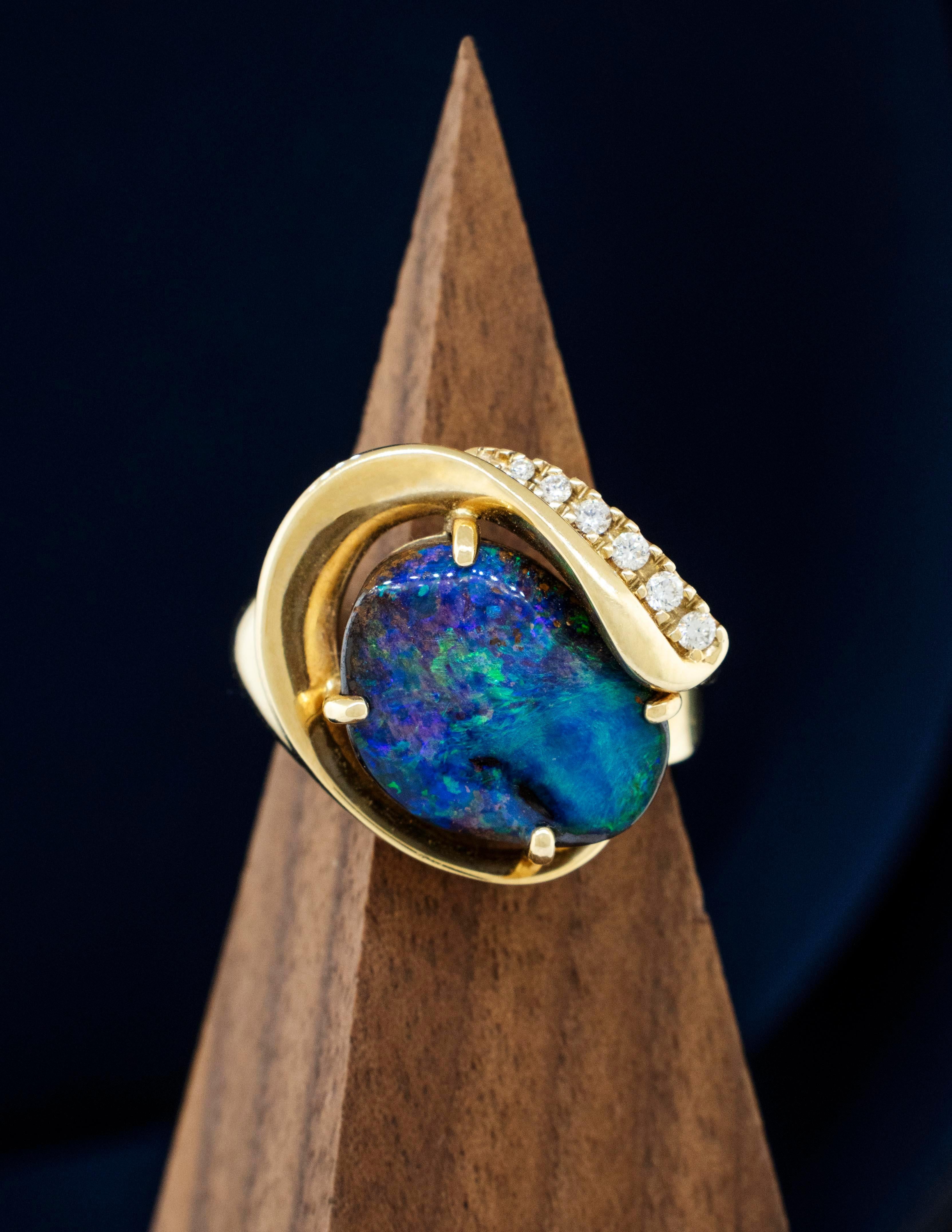 Raro Ópalo Negro Australiano con Diamantes Brillantes Redondos en un anillo de forma libre de Oro Amarillo de 14 Kilates. El ópalo negro natural tiene matices centelleantes de verde intenso, azules, morados y tonos dorados. Recuerda cautivadoramente