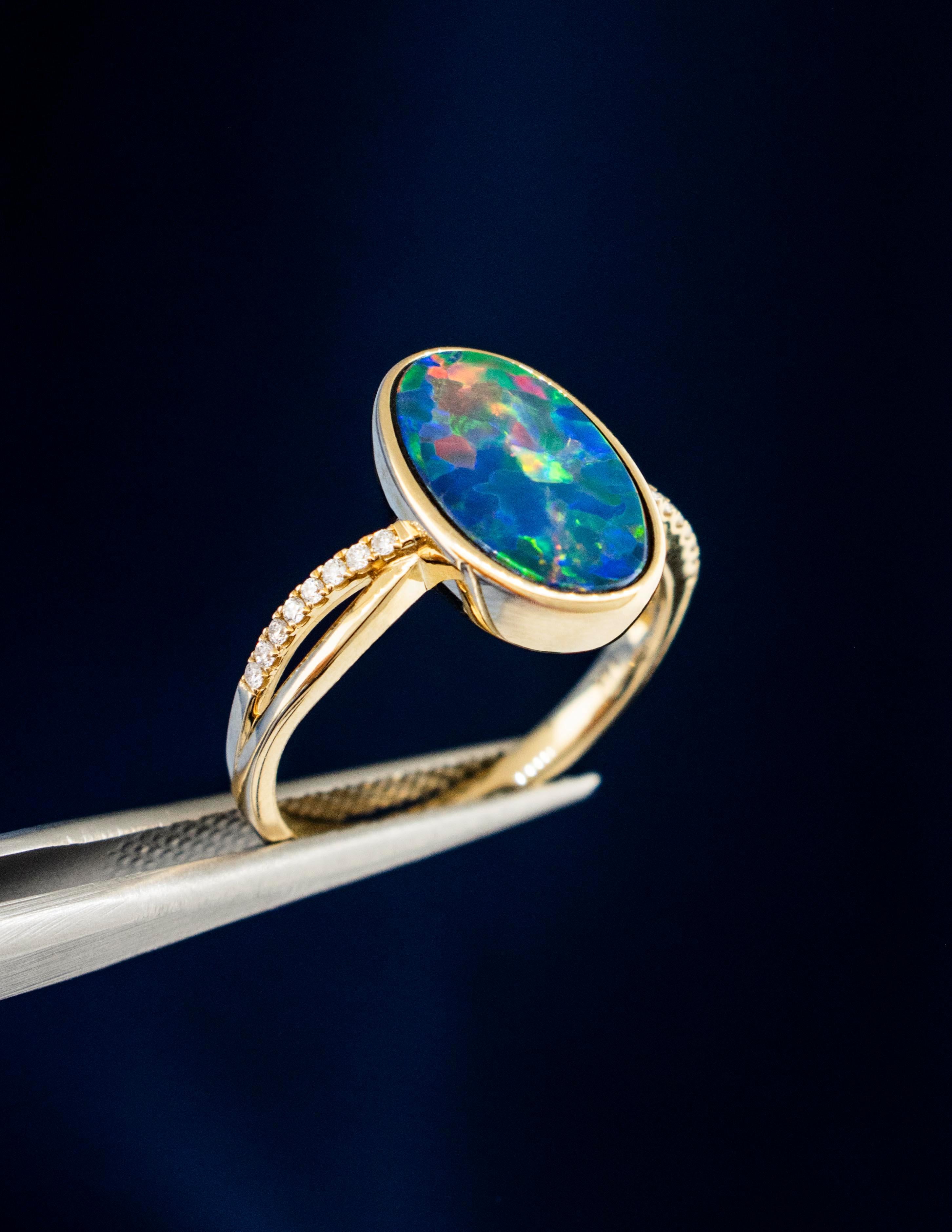 A 14K yellow Gold Black Opal Ring with Diamond accents. The Australian Black Opal is very scintillating with brilliant flashes of  Green, Blue, Purple and Fiery Reds. The Bezel Set  Oval shape Opal measures 13.14mm x 8.09mm x 2.7mm weighing approx.